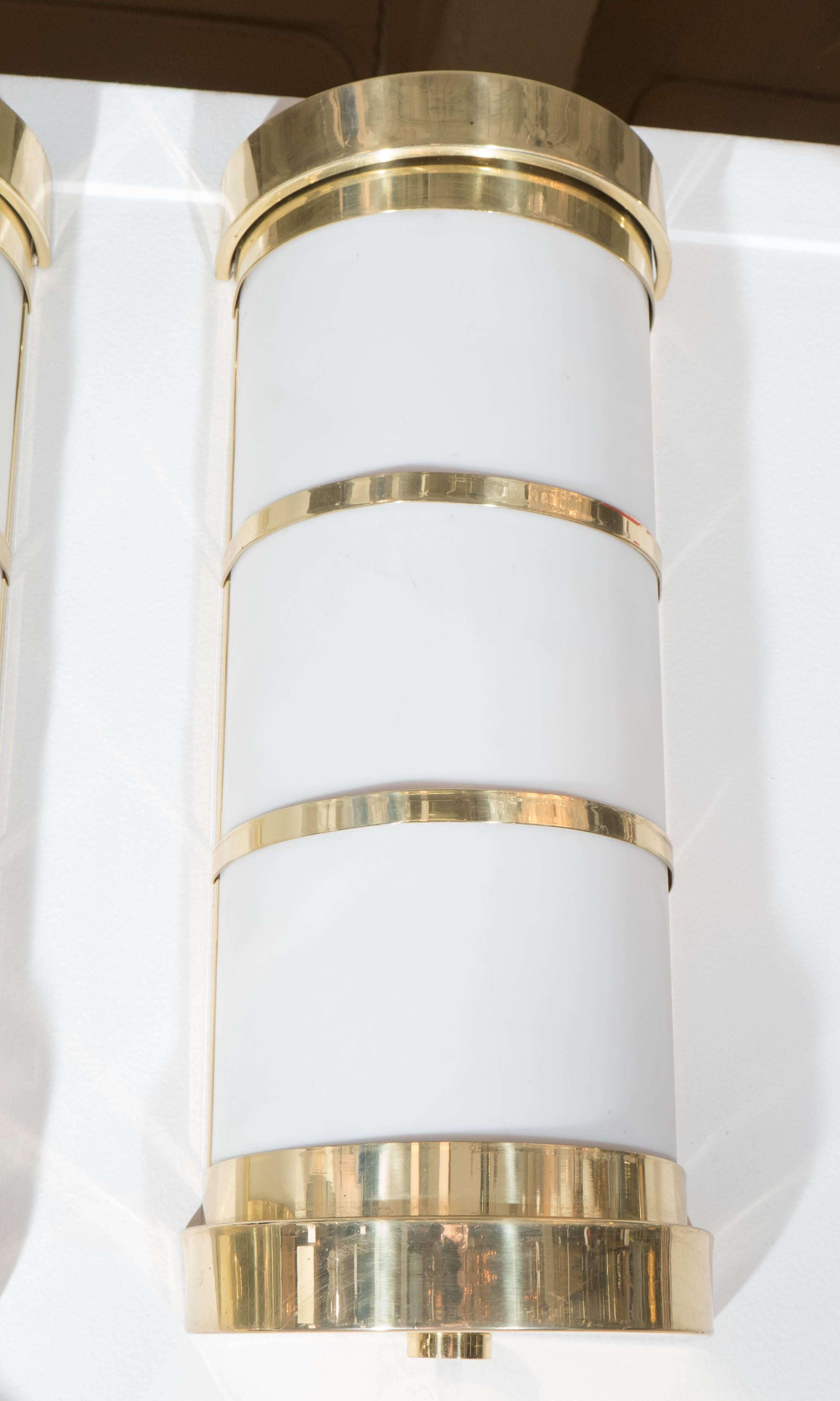 A pair of flush mount wall sconces, each with a cylindrical shade in frosted acrylic, with banding, top and bottom in brass. Other than light pitting and scratches to the brass, these light fixtures are in very good condition, consistent with age