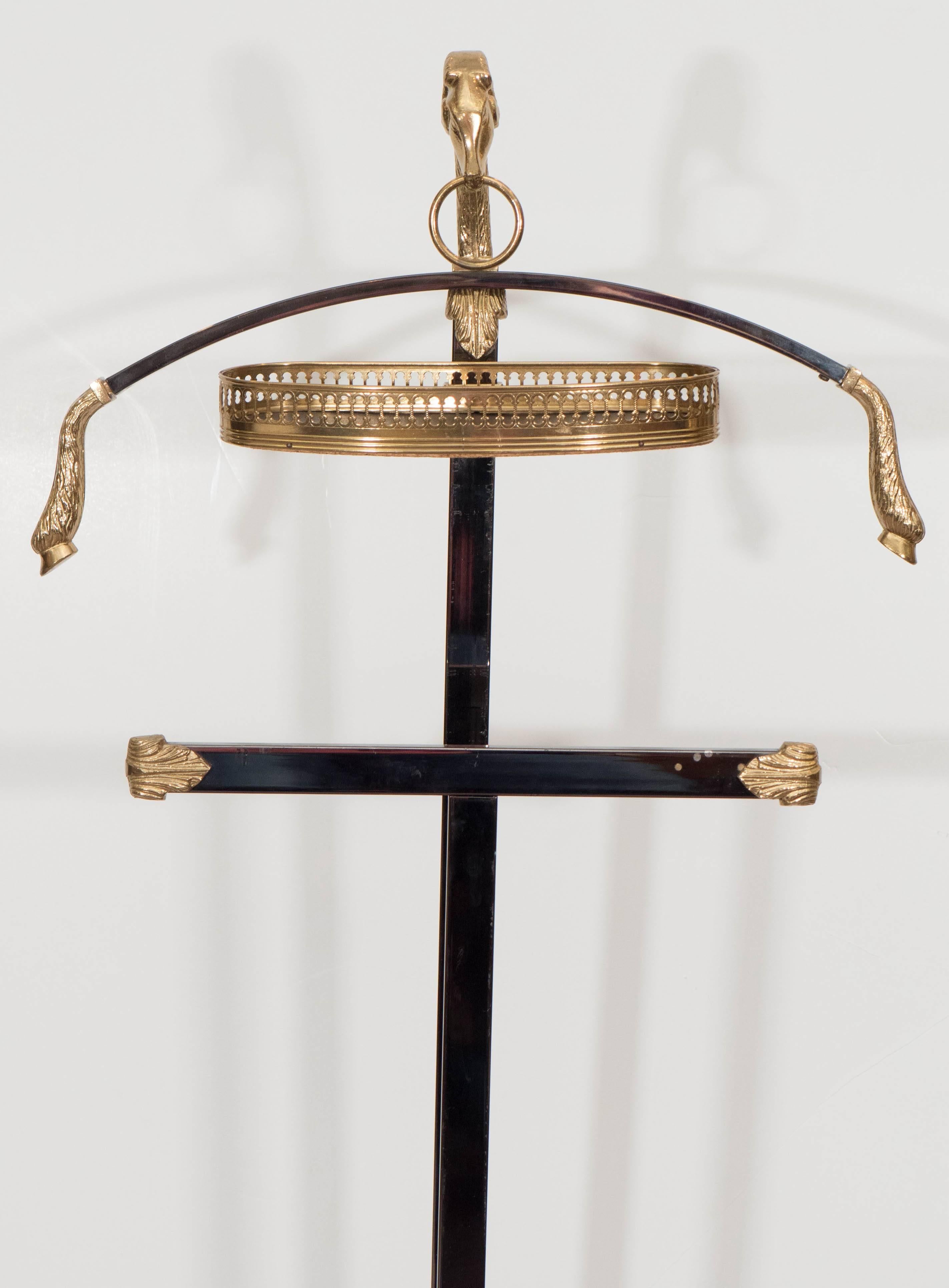 A Maison Jansen valet, influenced by neoclassical themes and produced in Italy circa 1960s, in polished dark steel and accented in brass, decorated with surmounted rams head and hooves to the shoulders, standing on tripod scroll form feet with