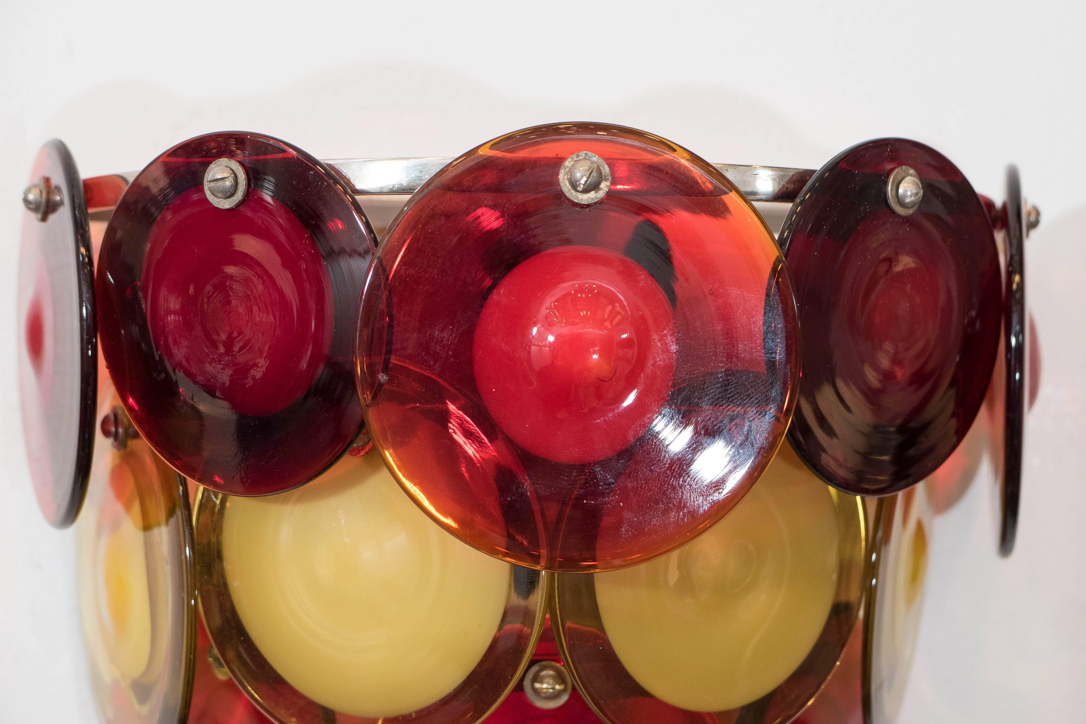 A pair of vintage sconces, each composed of three tiers of discs in brightly colored Murano glass, suspended from a demilune frame, produced by Vistosi of Italy, circa 1970s. Wiring to US standard. Both fixtures are in very good condition,