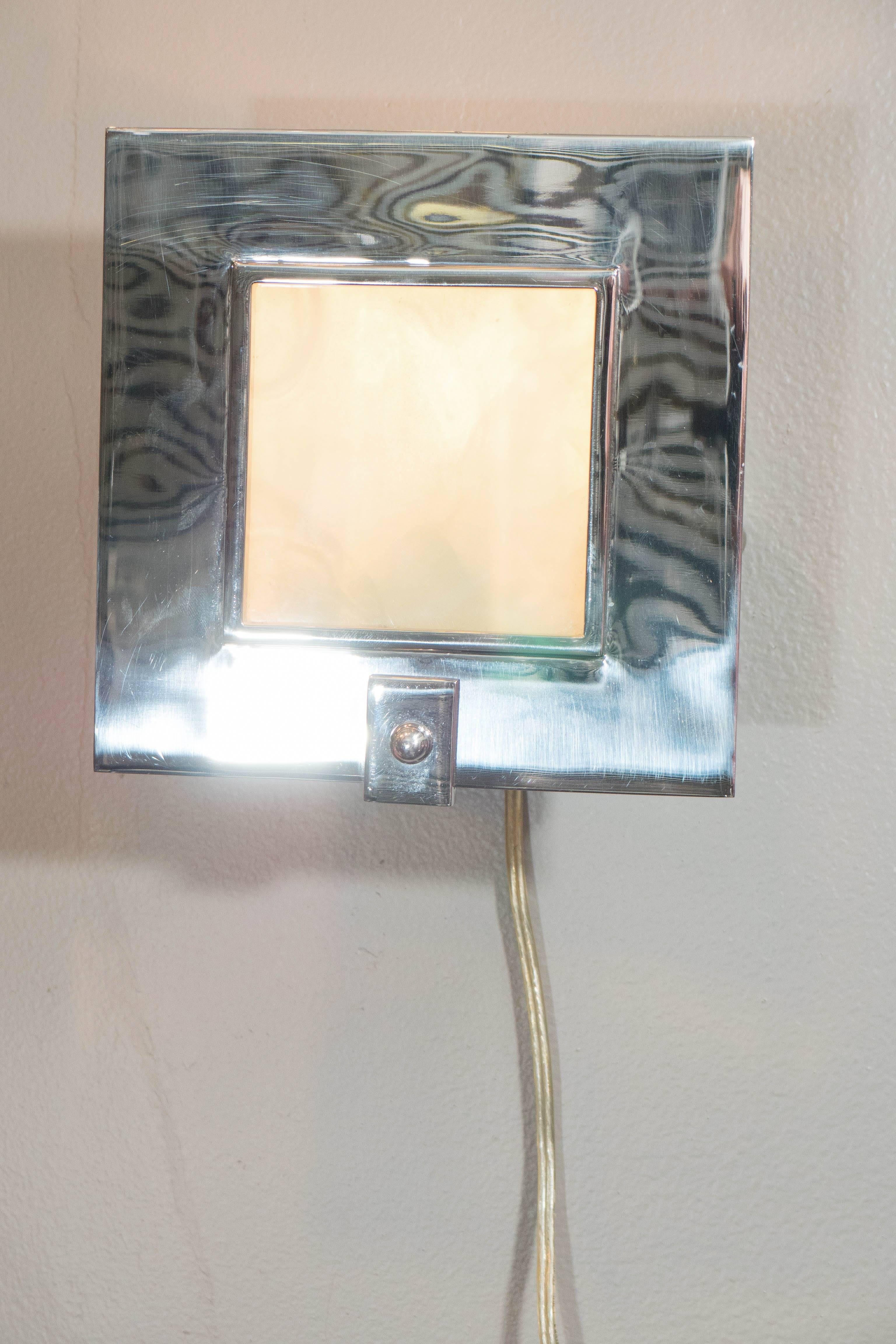 This pair of contemporary chrome wall sconces, produced by Theodore Alexander, founded in 1996 by Paul Maitland Smith, each includes a modernistic square shade, accented with glass, over a round backplate. Wiring and sockets to US standard, each