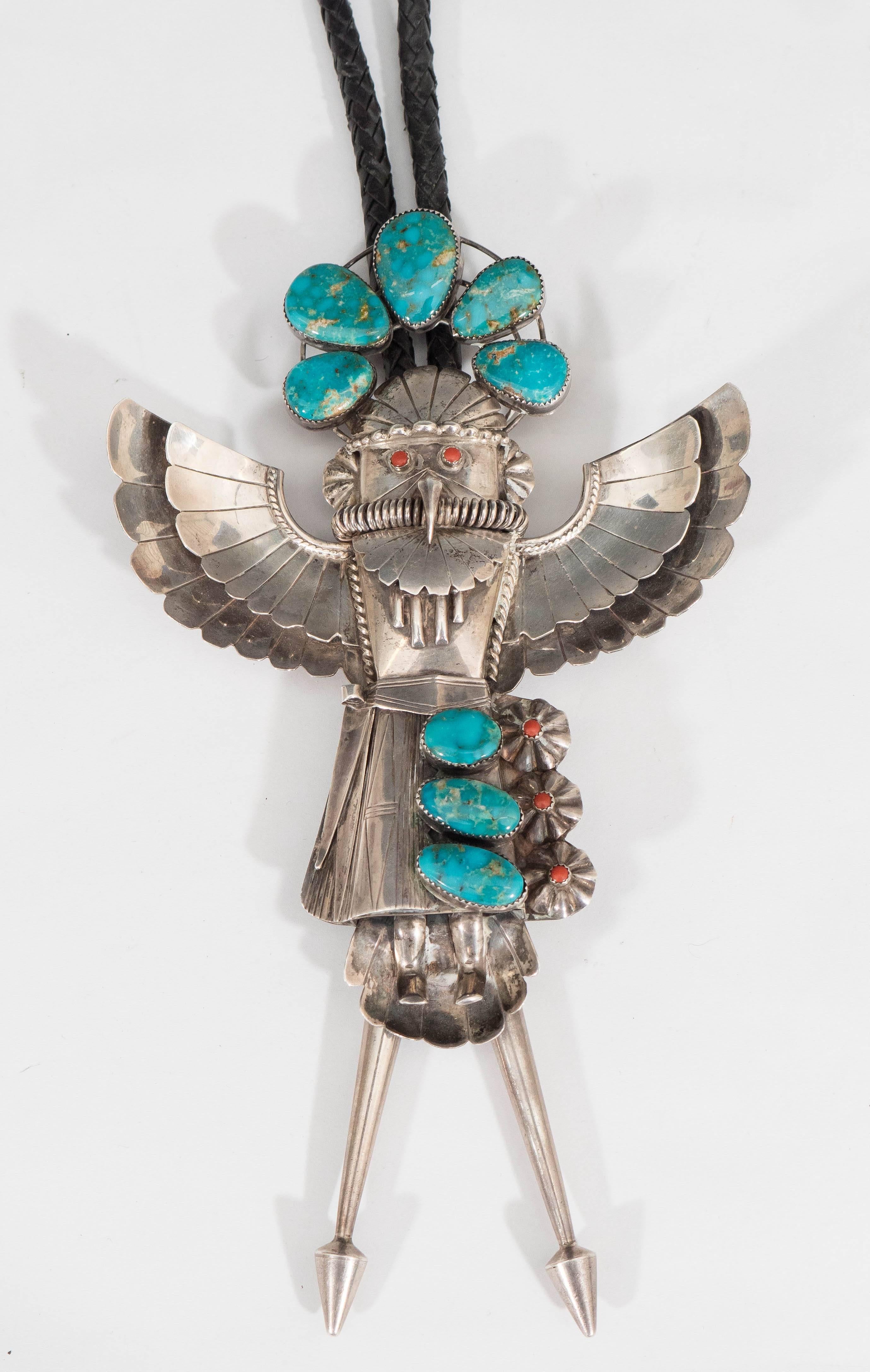 This huge and important Native American bolo tie necklace, depicted as a kachina, comes in sterling silver, with black braided leather, accented with turquoise and coral. Markings include artist’s monogram to reverse. Excellent condition, consistent