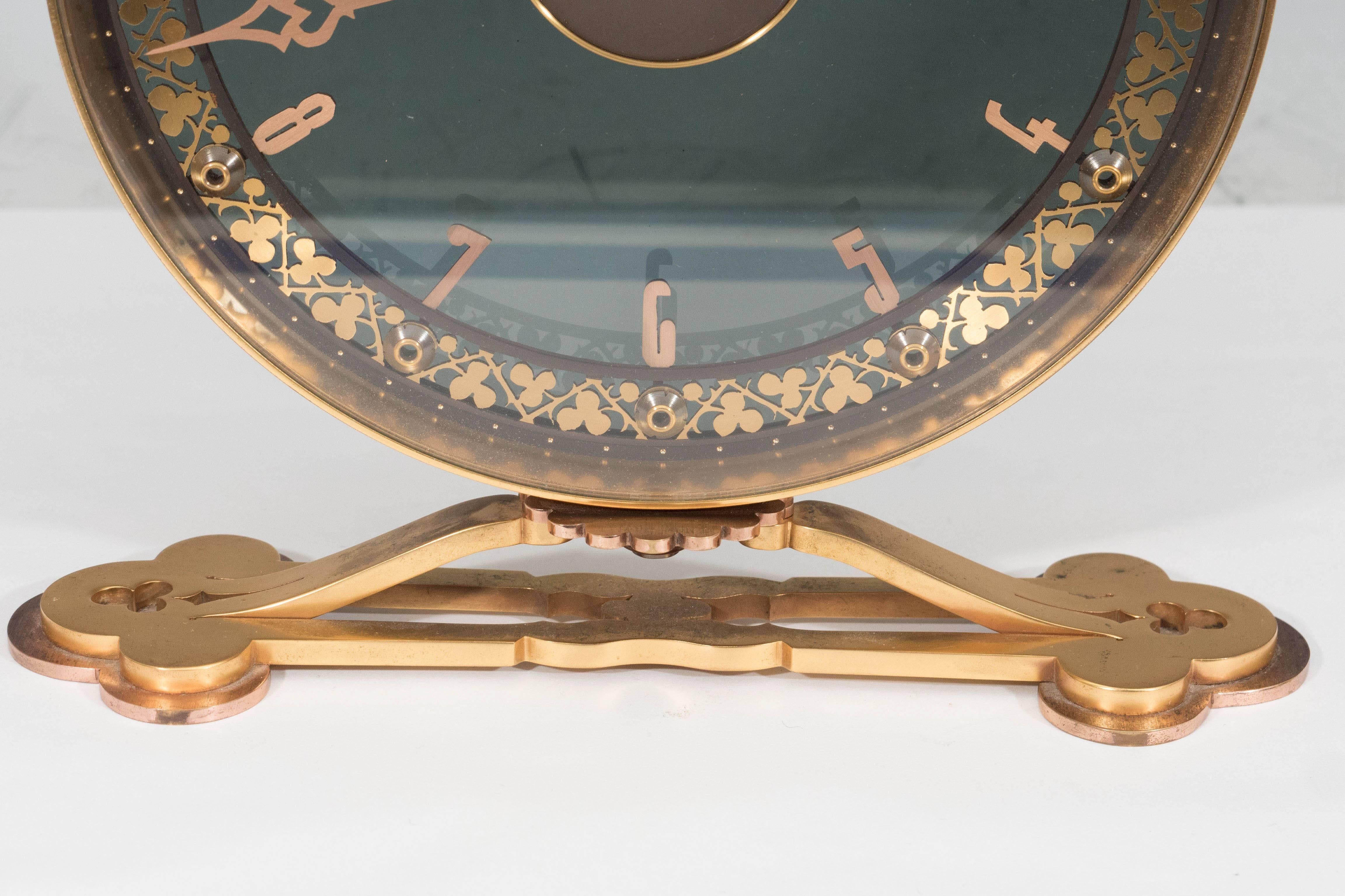 This gorgeous eight-day skeleton desk clock, produced in Geneva Switzerland, circa 1950s by Jaeger-LeCoultre, comes with a round face in smoked glass with Arabic numerals, the border detailed with a pattern of clover-leaf, inset within a brass