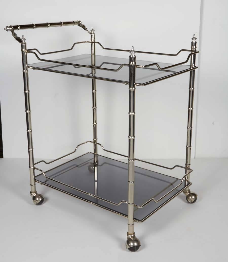 Mid-century modern bar cart with two-tier design. Features elegant bamboo motif, with matching handle and finials, in a polished chrome finish. The serving cart if fitted with smoked grey glass shelves and stylized chromed galleries or safeguards,