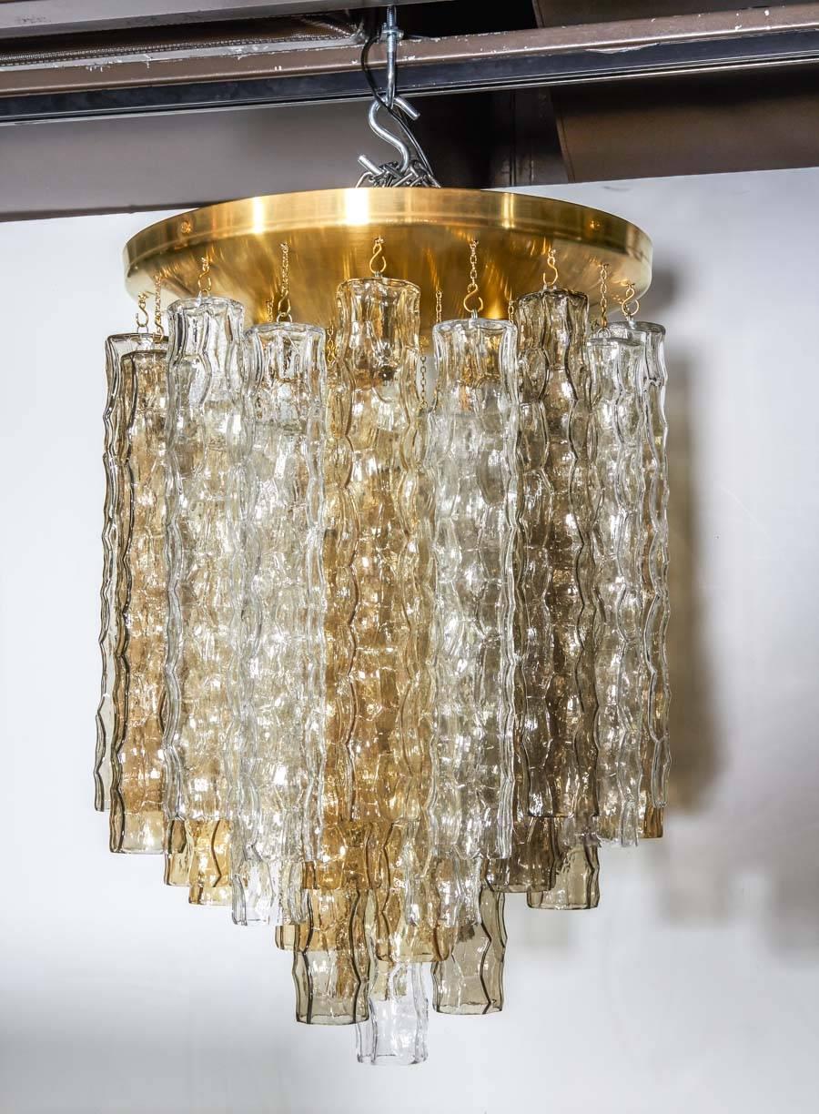 Mid-century modern chandelier comprised of three tiers of handblown Murano glass pendants with bamboo texture and design. The glass pendants come in alternating colors (smoked grey, amber, and clear). Features a large brass dome ceiling plate with