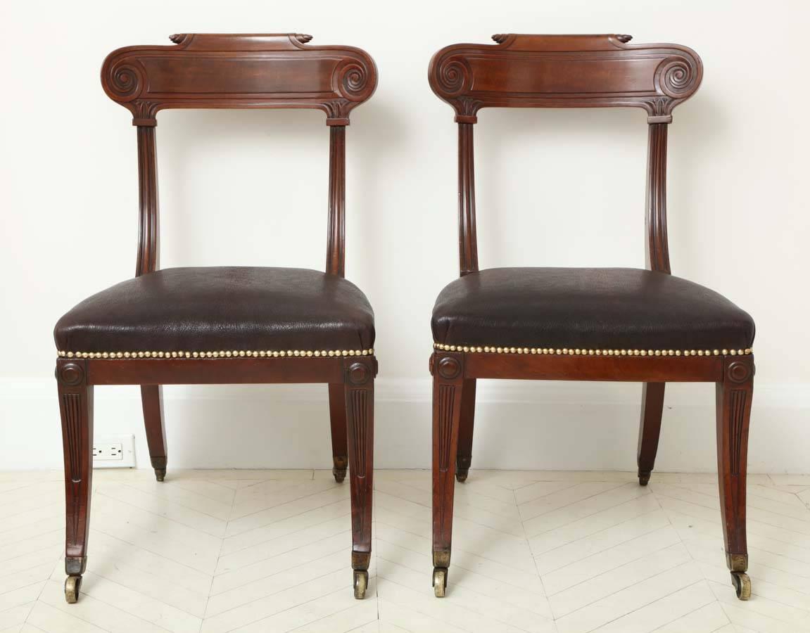 A pair of English Regency mahogany side chairs with carved back rails above fluted supports and sabre legs, circa 1815.