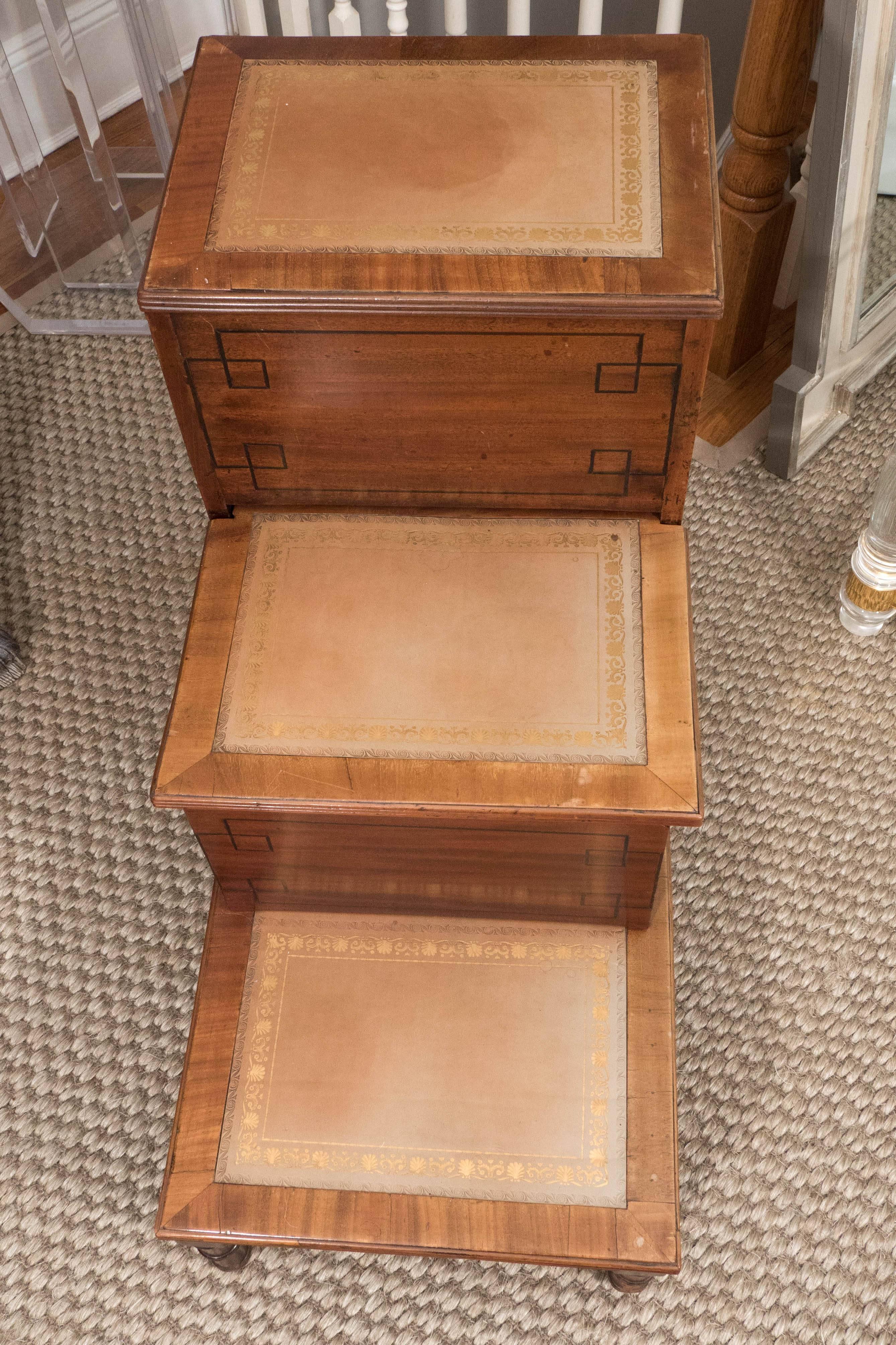 A handsome set of library steps in light mahogany with a lovely tan tooled leather, ebonized inlaid design on front of steps and reeded detail on base and tops of steps. The piece includes two storage compartments. This piece, from Belgium. Has both