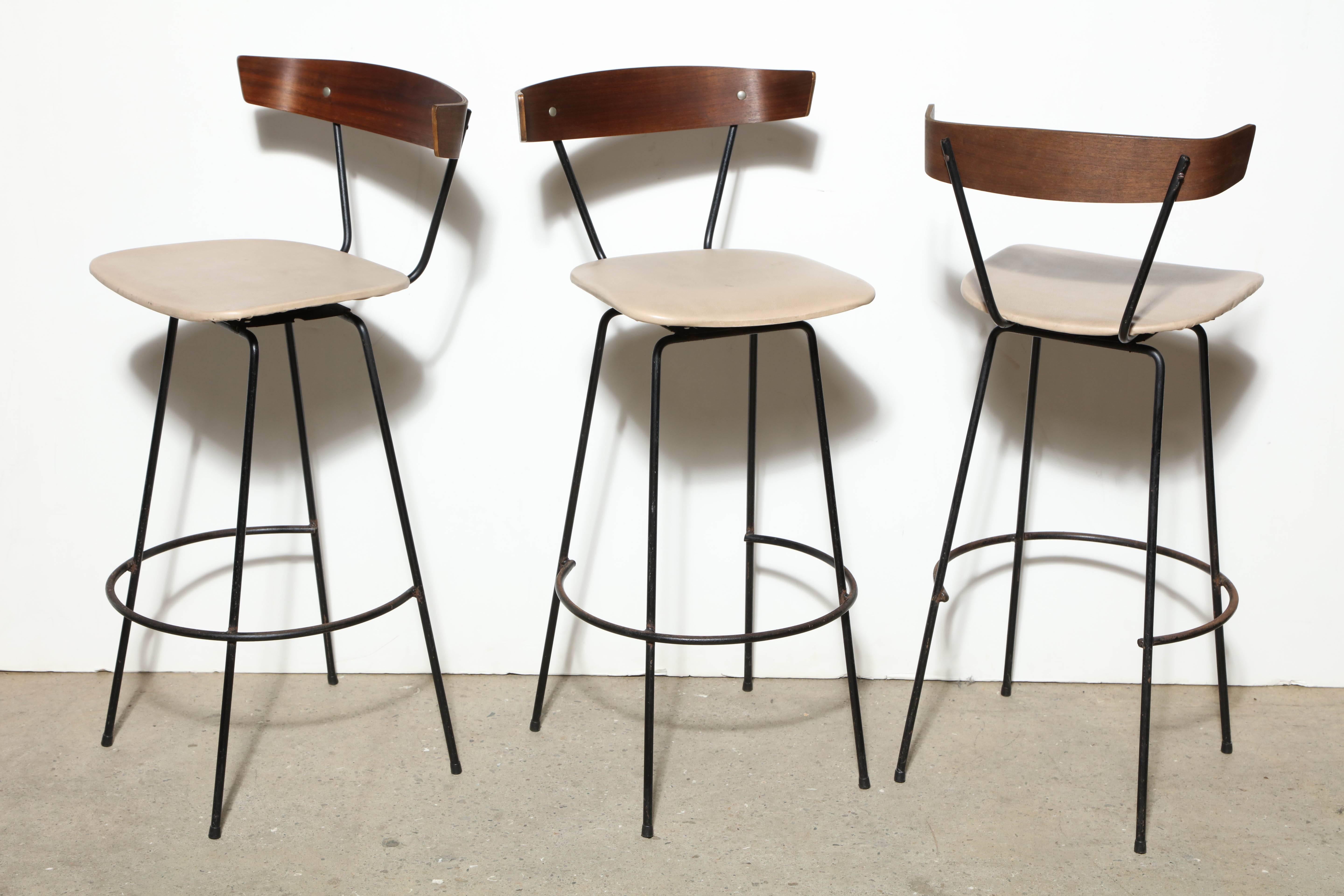Three MCM 1950s Clifford Pascoe for Modern Masters Inc. Bar Stools with open black wrought iron legs and footrest, comfortable and rounded, molded mahogany backs with swivel cream vinyl covered wooden seats.