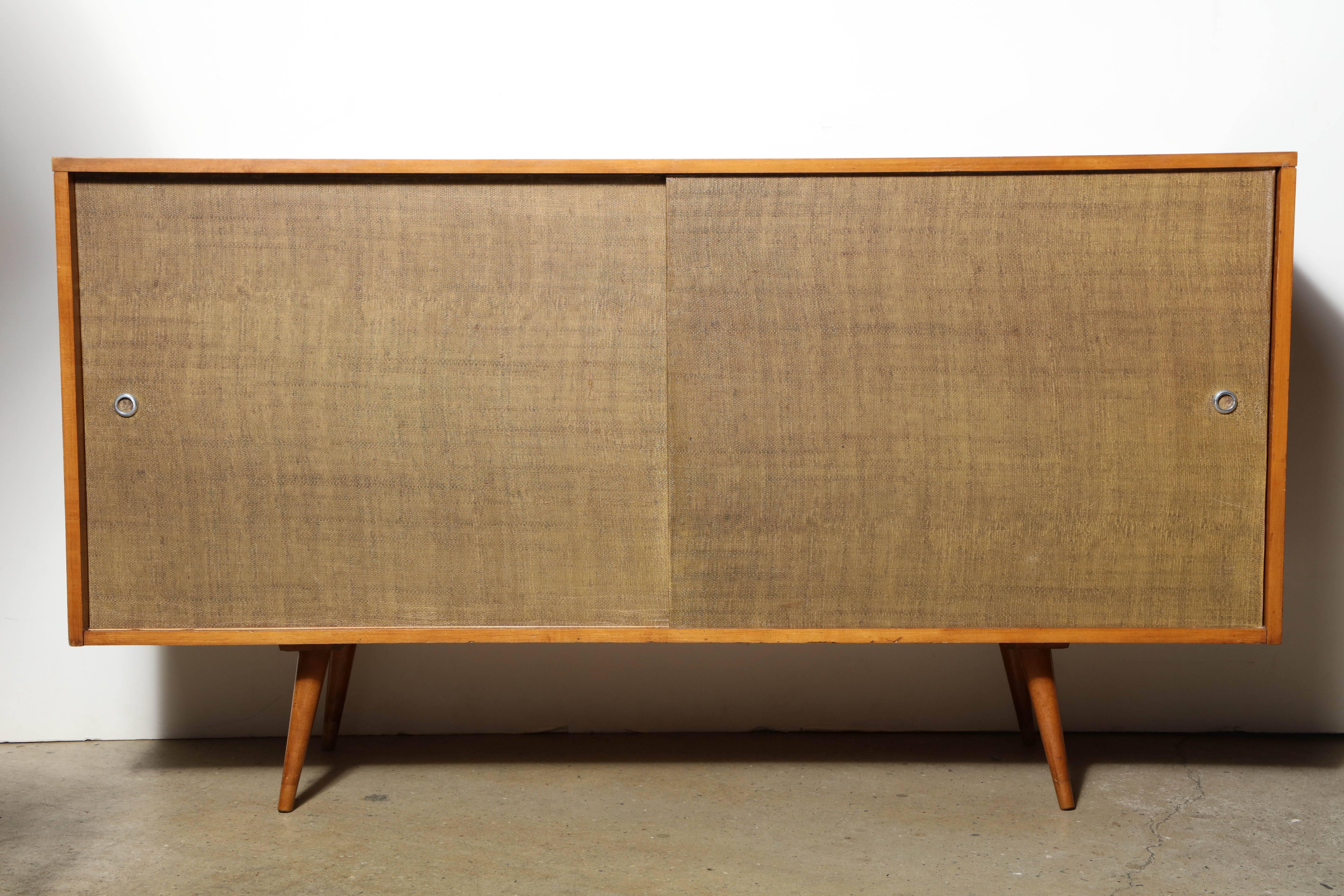 Mid Century Modern Paul McCobb Planner Group for Winchendon Maple Two Door Buffet Cabinet. Featuring a solid Maple frame, Two grass cloth covered sliding doors on four splayed legs. Includes three right interior drawers with one left drawer and