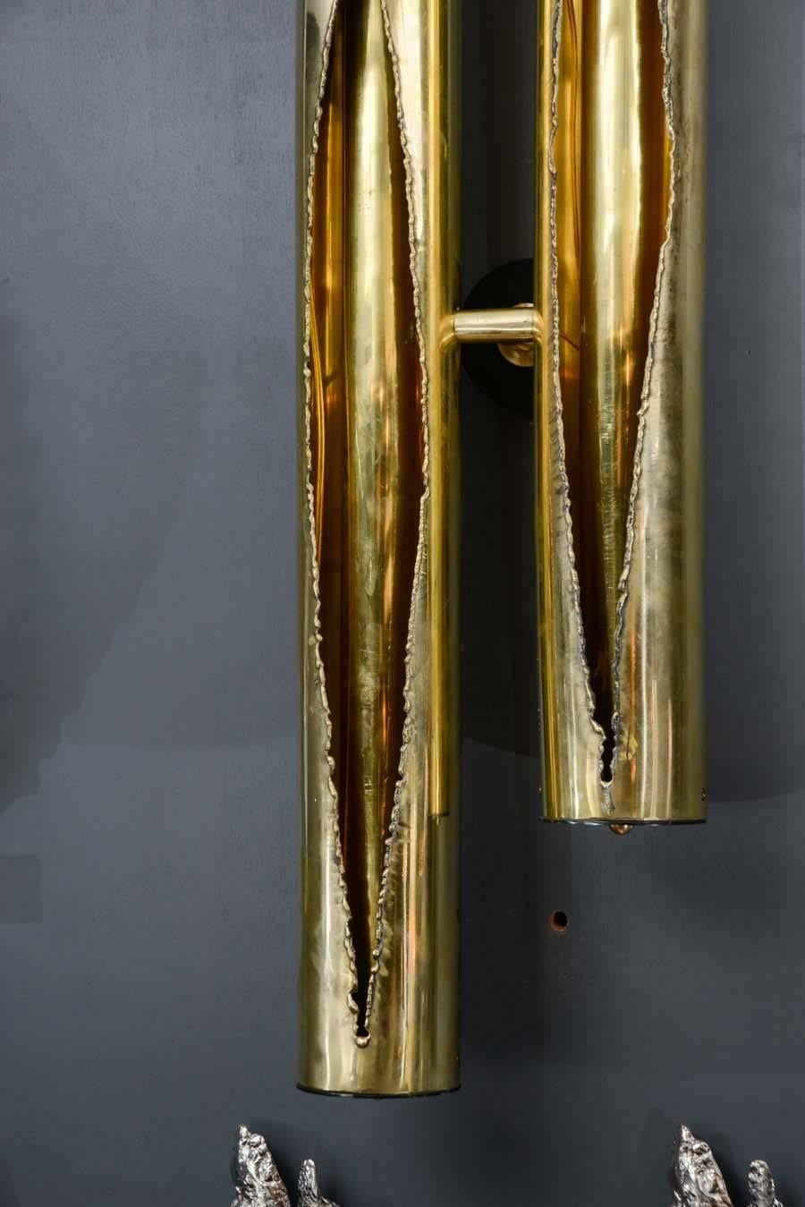 Exceptional set of wall sconces made of brass with black metal settings.

The sconces are made of two tubes looking like they were cut open to reveal the inside which is an other tube hiding the light sources.