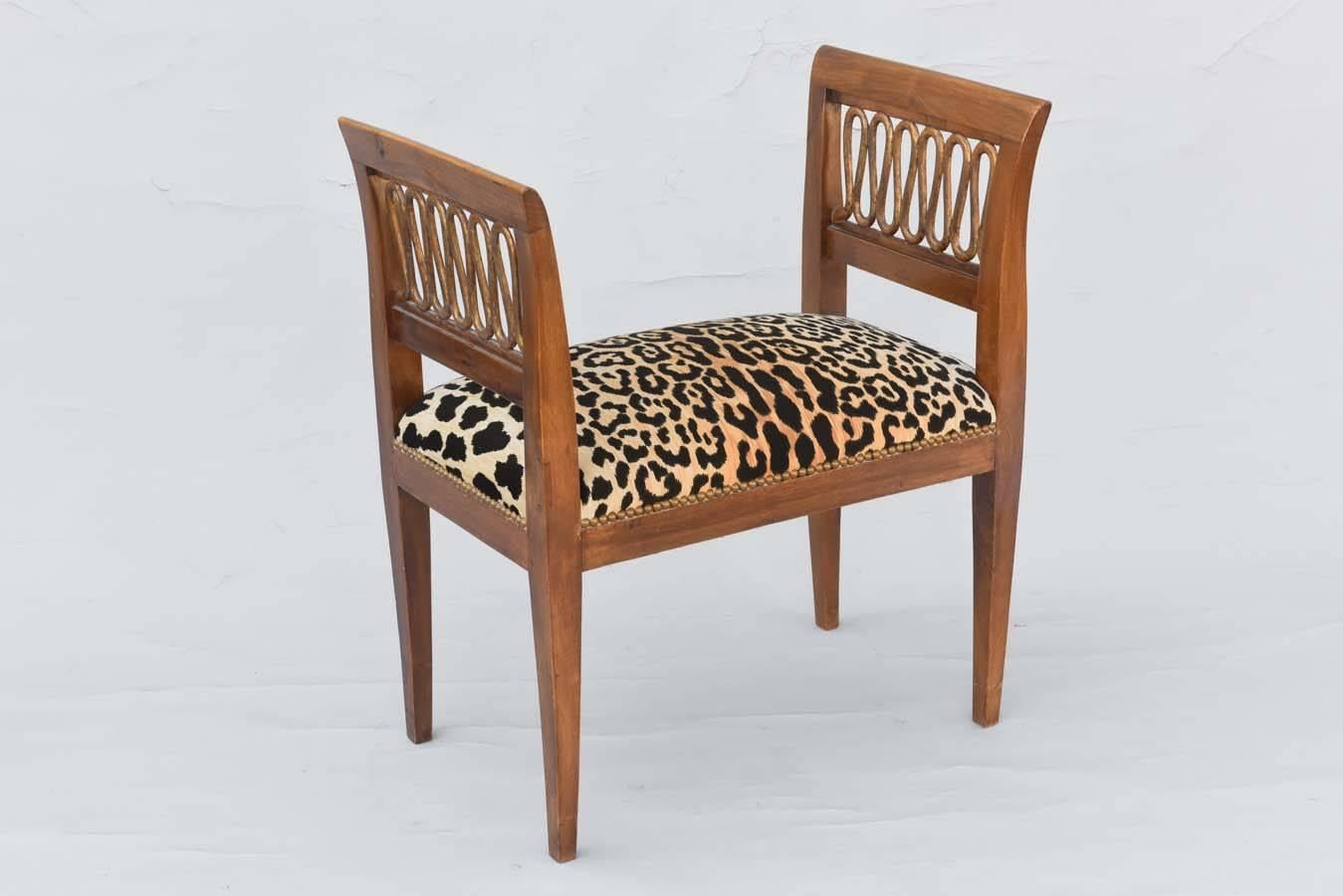 Bench, having a crown seat of leopard print fabric, with nailheads, flanked by square, flared arms, inset by pierced and gilded looping fretwork, raised on square-section, tapering legs. Upholstered in leopard print velvet, with nailheads. 

Stock