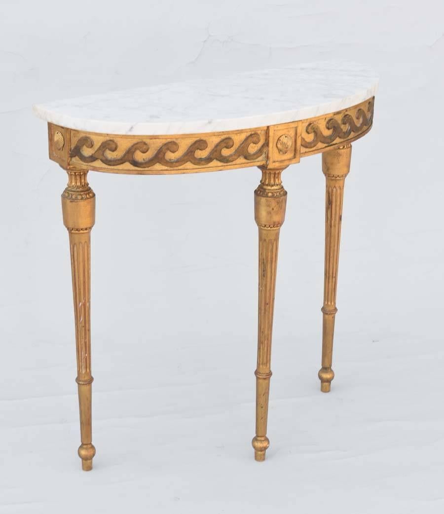 Console table, having a D-shaped top of Carrara marble, on giltwood base, its apron outcarved with an evolute scroll, centered by a framed scallop shell, raised on round, tapering, stop-fluted legs, ending in touipe feet.

Stock ID: D9291