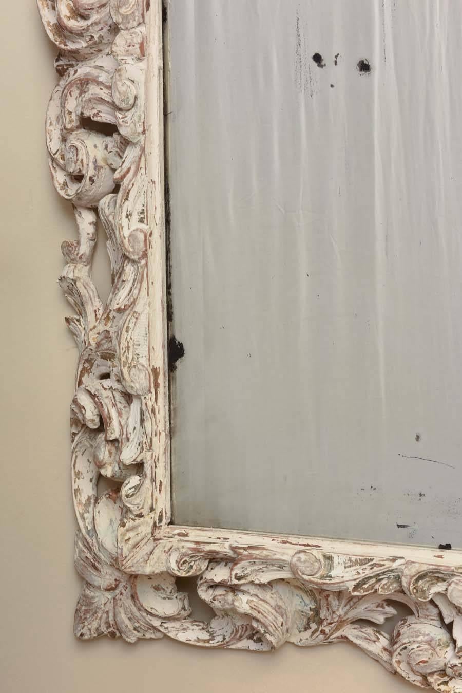 Mirror, having a pierced, rectangular frame of carved scroll work and acanthus leaves, its distressed finish with bits of parcel-gilt, holding a bevelled mirror plate with natural wear and spotting.

Stock ID #D9297