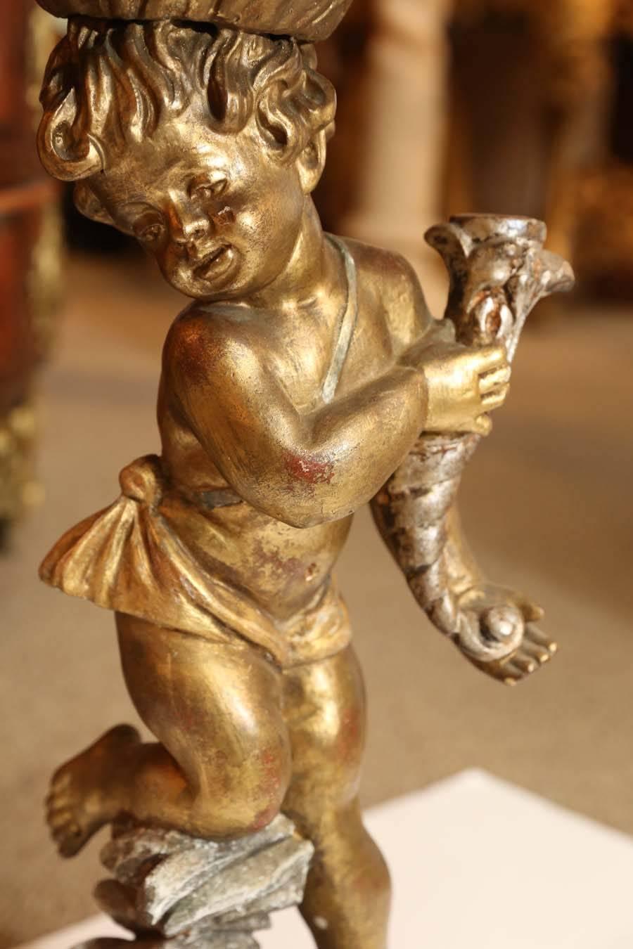 Antique Venetian table in giltwood and faux marble.
A statue of a putti supporting a tabletop in faux gold marble.
Posed on faux rock base and holding a cornucopia in his hands.