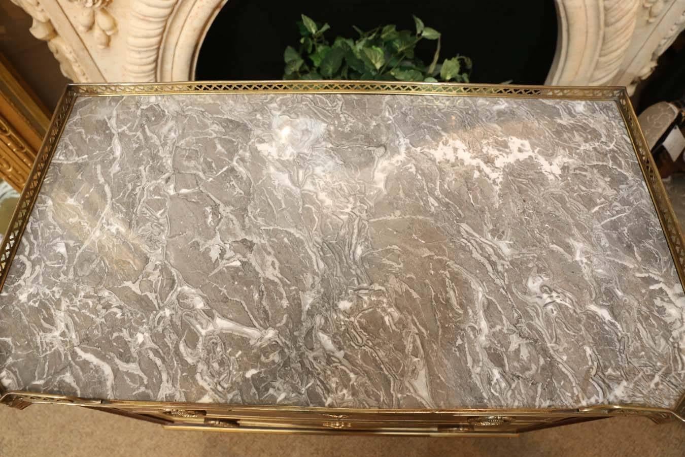 Rectangular marble-top commode with a three-quarter pierced gallery and
canted corners. The case is fitted with two drawers, each with brass
banding, raisedon tapering square legs ending in tall brass caps.
Pale gray and white marble.