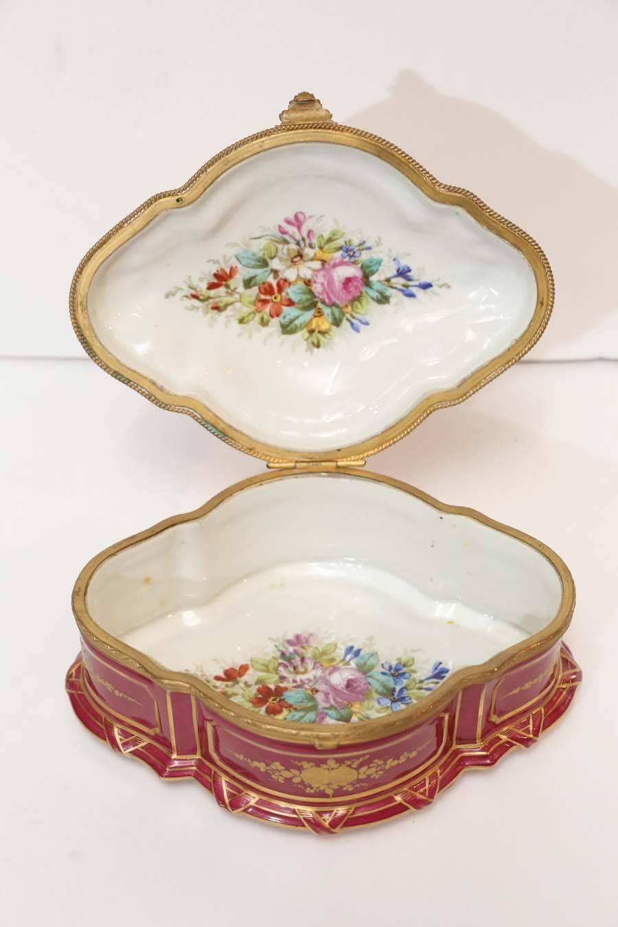 19th century French Sevres porcelain box.
In cranberry color with painted garden scene.
Oval in shape with gilt painted designs on all sides.
 