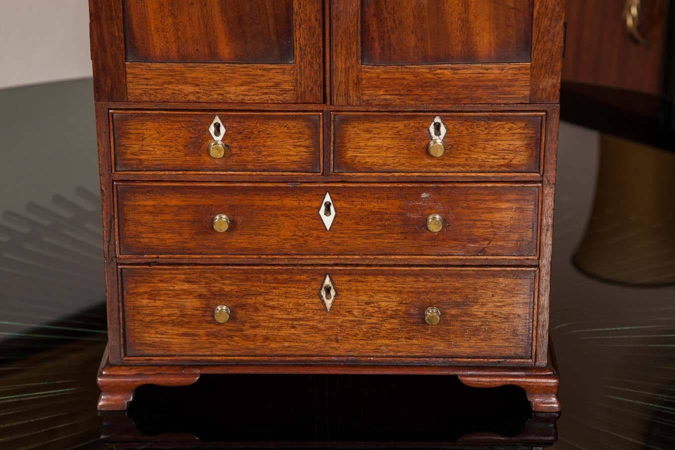 A wonderful Georgian mahogany model of a linen press. The upper doors opening to reveal two linen slides above two over three graduated drawers on ogee bracket feet; the top crossbanded.
The ivory escutcheons suggest a West Country origin.