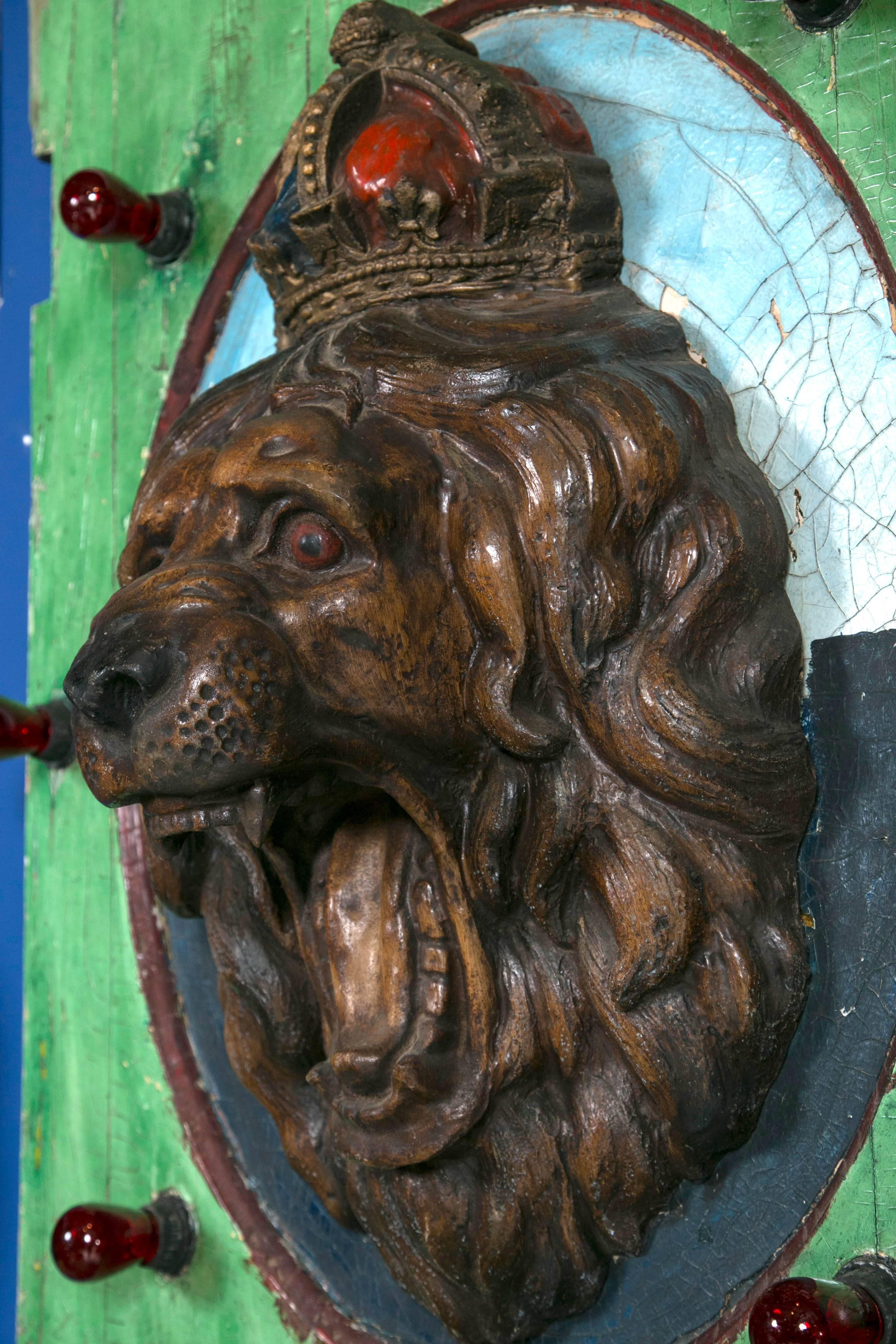 Early 1900s lion's head, wooden panel section from a carnival or traveling circus carousel. Bright carnival colors on the wooden panel surround a lion's head in relief with a ring of lights around the rim. Recently rewired from the original cloth