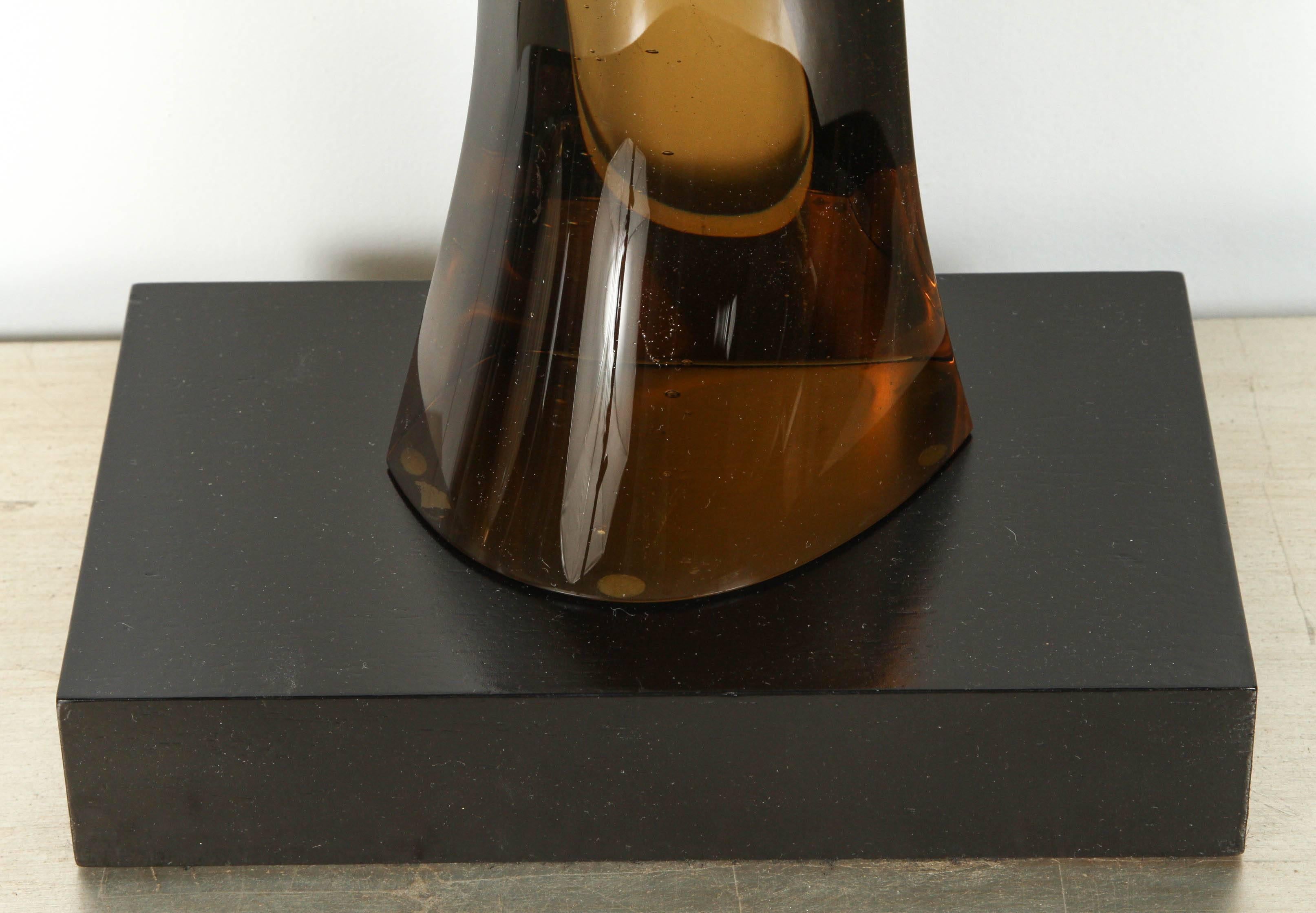 Sleek 1970s smoked glass sculpture set on a black wooden base. 
The smooth glass undulates and tapers up from the base. It fades from a dark amber to nearly clear at the top.