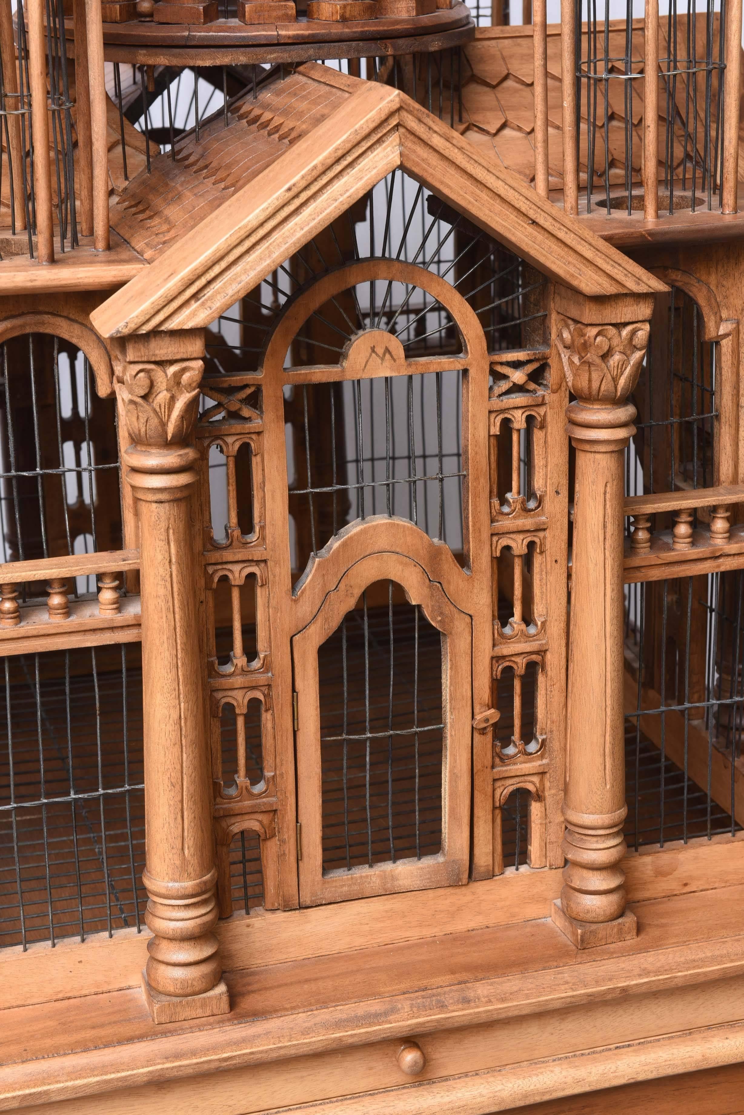 Large and impressive carved wood pavilion birdcage with doors on each side and pull-out tray. Birdcage rests on a matching table base.