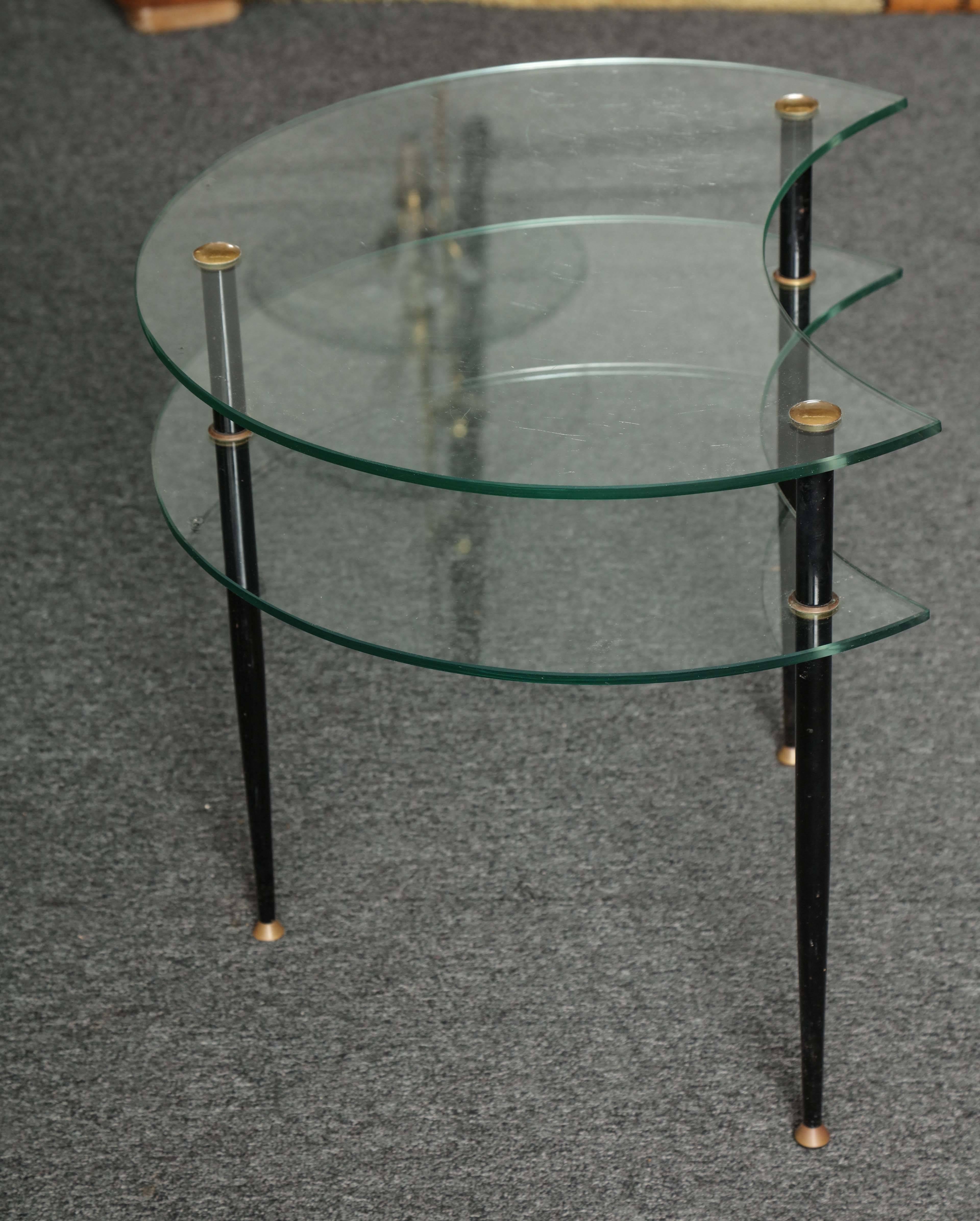 Stylish side table made in Milan, 1960 by Vitrex, designed by Eduardo Paoli, two crescent shaped shelves on three black enameled and brass legs, unusual.
 