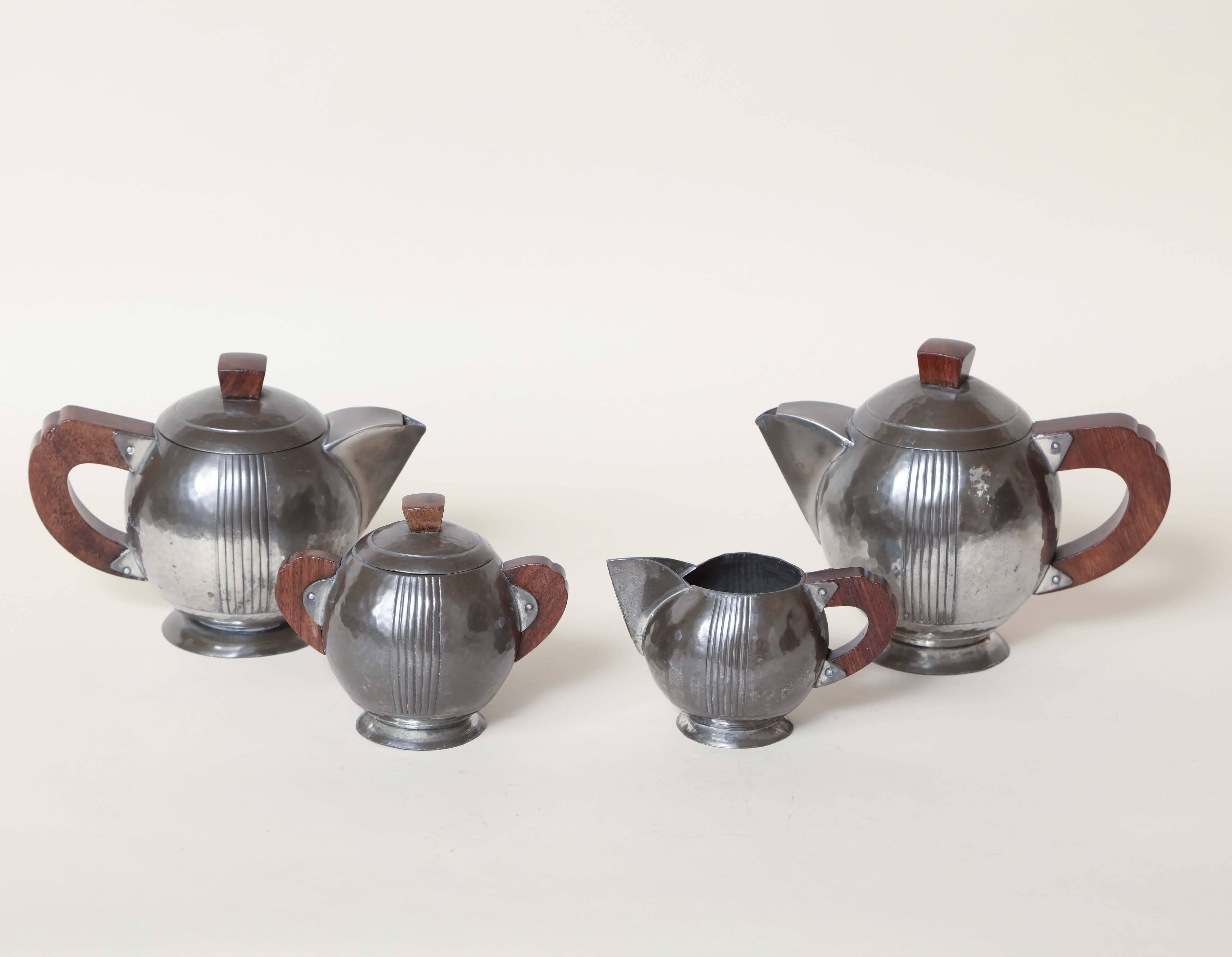 Hand-wrought dinanderie pewter martele coffee and tea service with vertical lines on body and rosewood handles and finials.

Measures: Teapot: 6 5/8'' high, 8 1/2'' wide, 4 ½'' long.
Coffee pot: 5 ¾'' high, 8'' wide, 4 ½'' long.
Sugar bowl: 4 ¾''