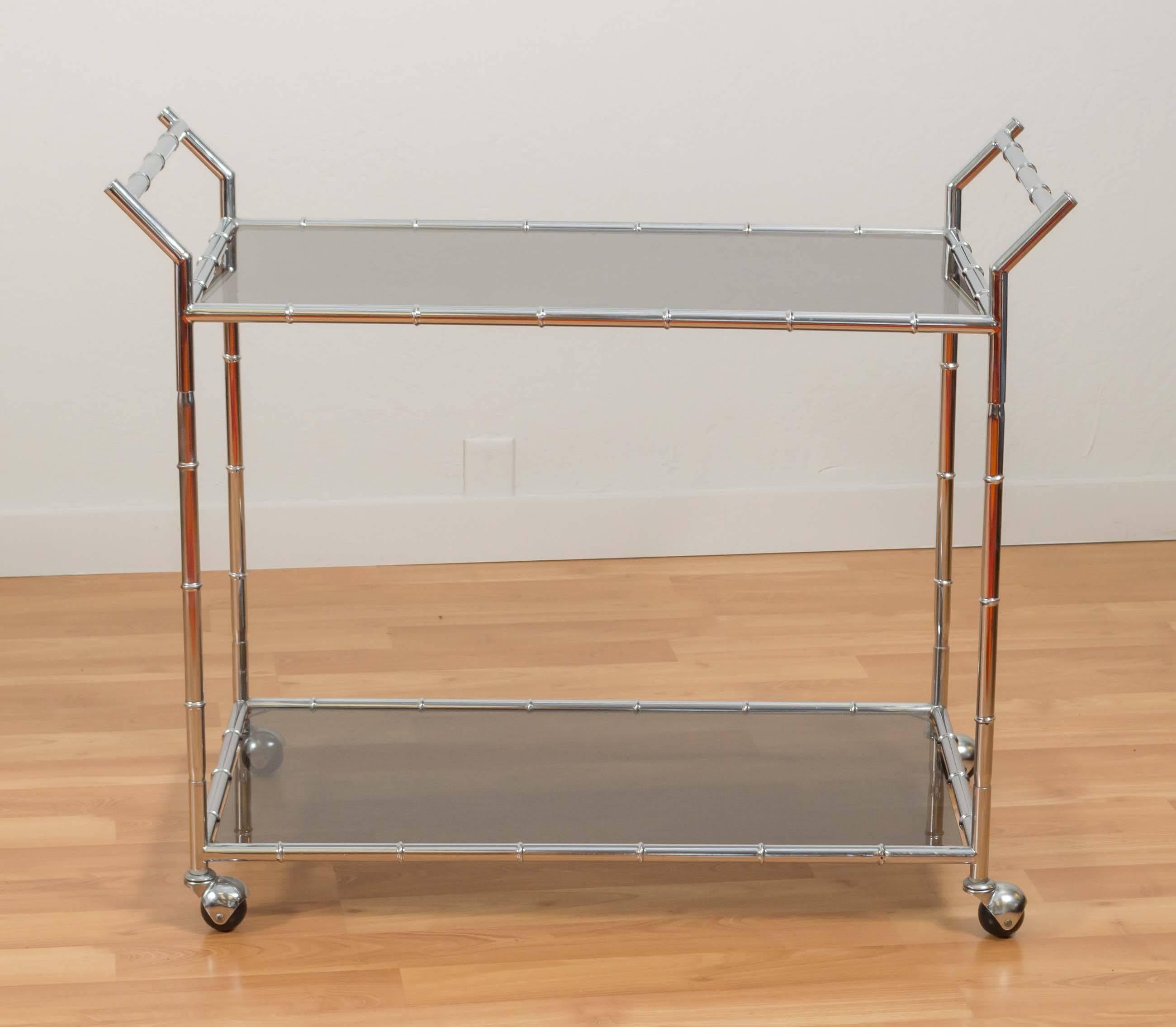 A Hollywood Regency-style faux bamboo chrome serving or bar cart with smoke glass shelves.

Its impeccably-fabricated and finished dual-handle chrome frame is in very nice condition over all, and it navigates smoothly on metal hooded ball casters.