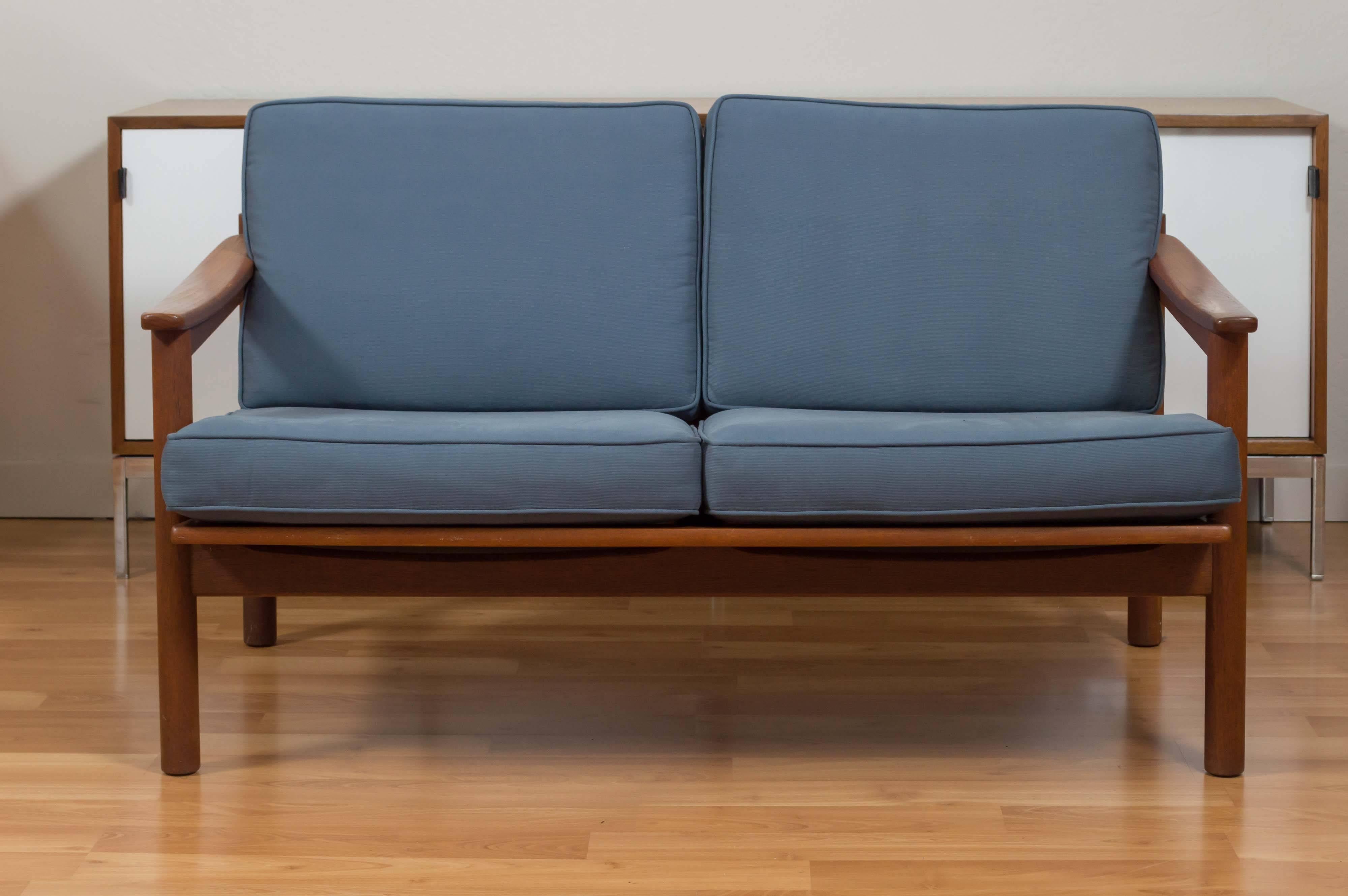 Perfectly proportioned compact teak sofa or settee with recently re-upholstered blue cotton cushions, with springs covered with rubber under. Quintessential Danish design combined with traditional Japanese craftsmanship, as evidenced by its