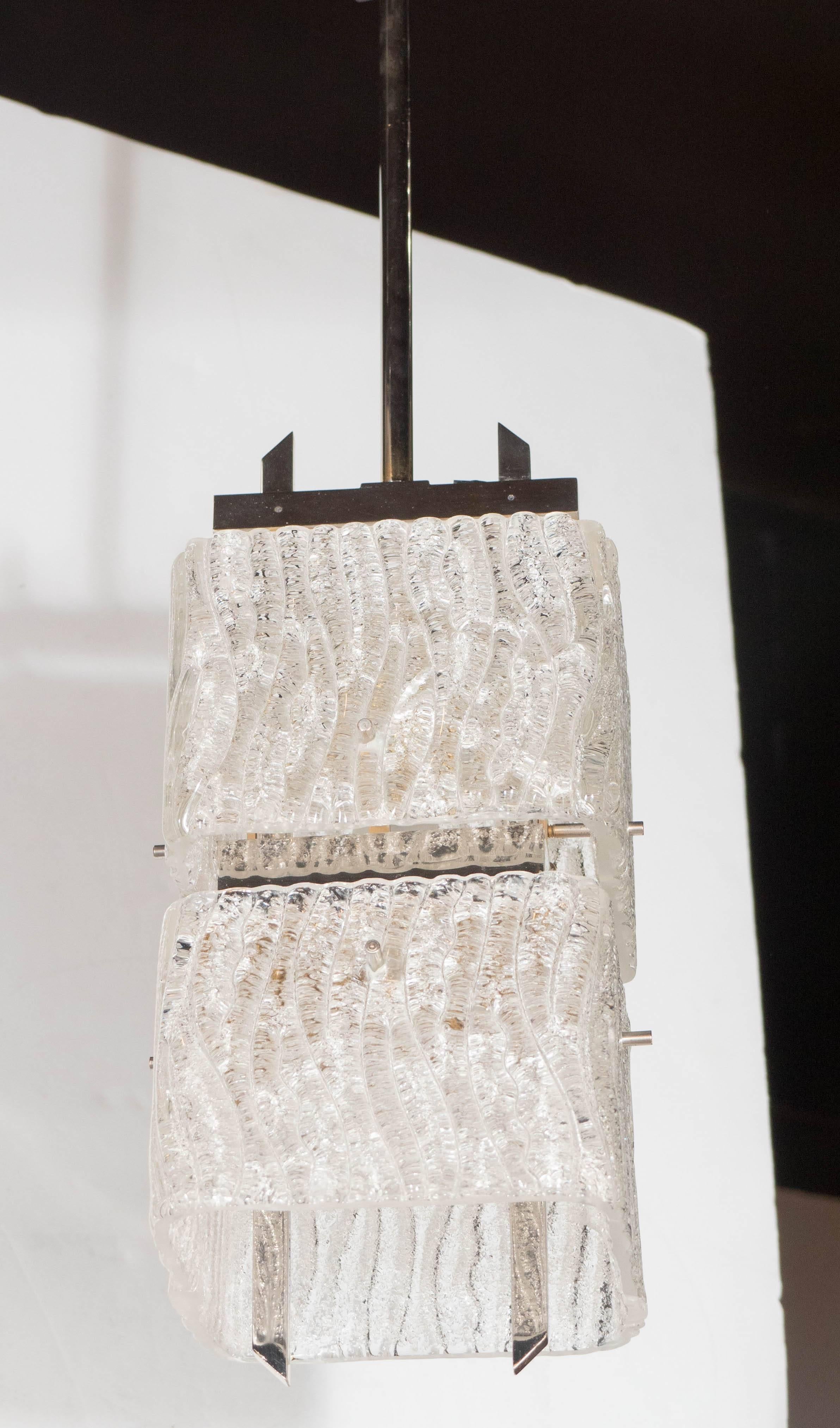 A Mid-Century Modernist two-tier textured glass pendant. Two round-edged square shades are supported by a chrome frame and fittings. A pair of angled chrome bars protrude from the top and bottom of the piece. This piece has been completely rewired