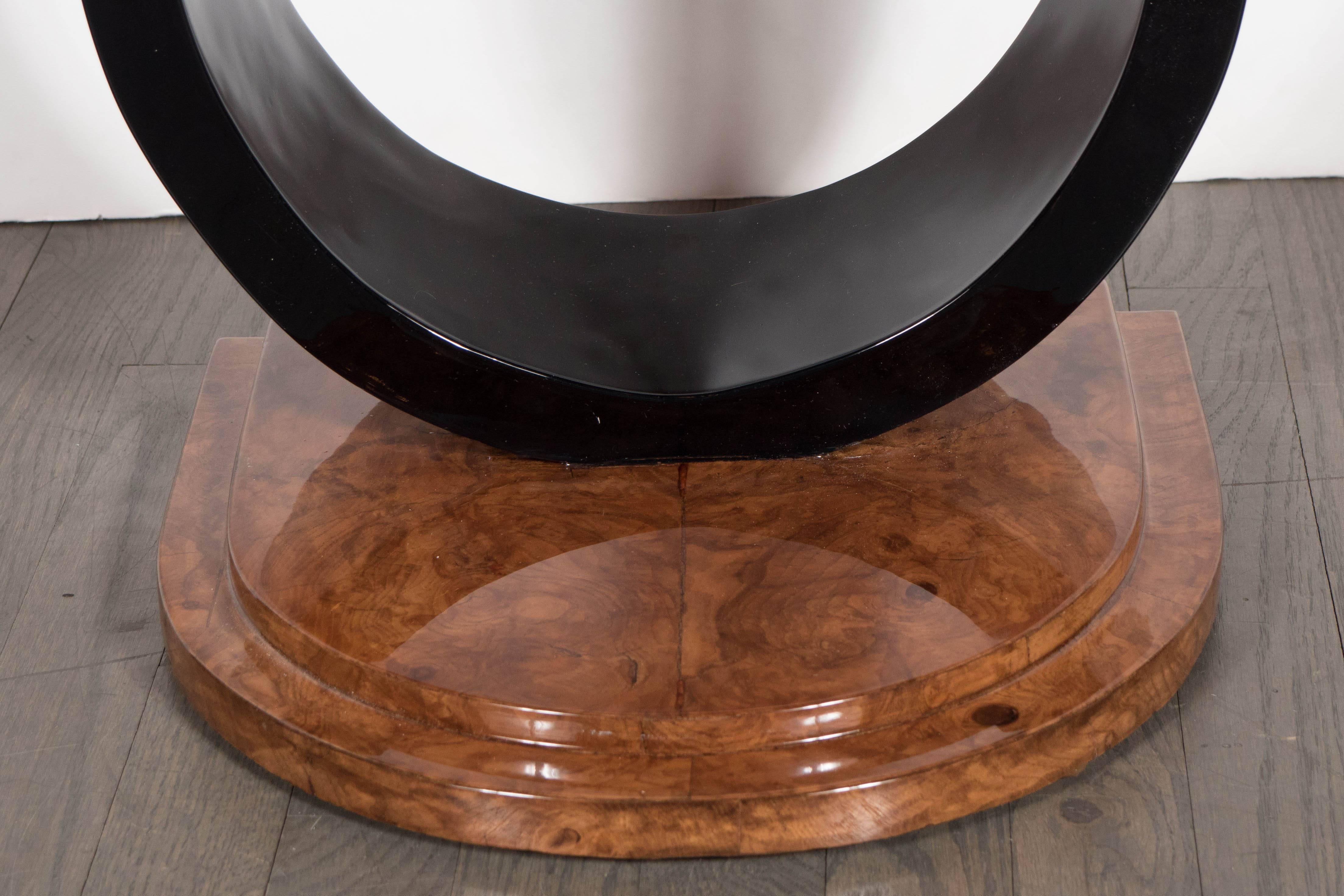 An Art Deco machine age occasional or drinks table by the Modernage Furniture Company. It features an exaggerated U-form stand in black lacquer on a stepped demilune burled Carpathian elm base. Nestled between the upper structure of the U-form stand