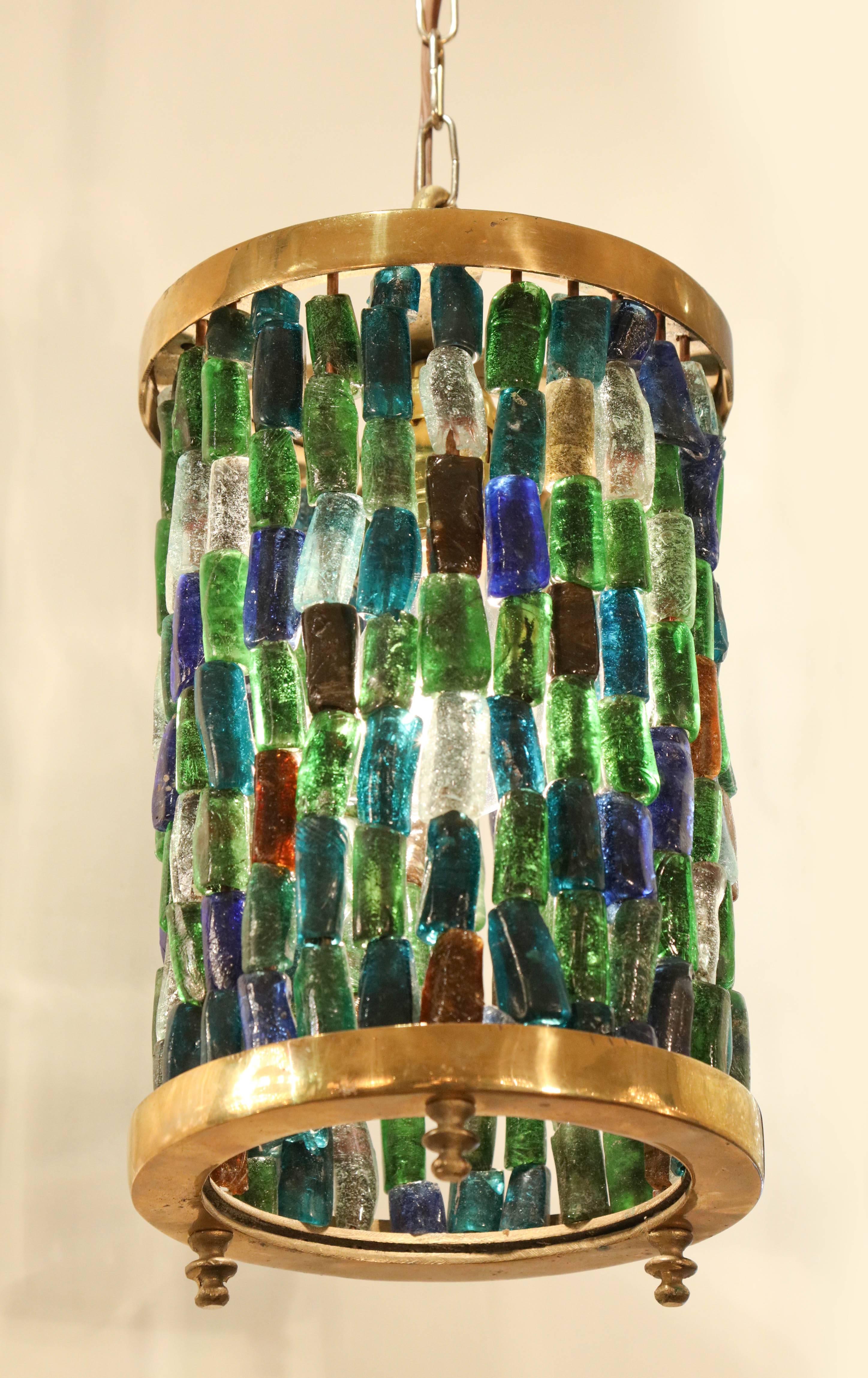 A lovely small lantern composed of a brass cylinder and small pieces of colored glass in stunning shades of blue, green, amber and clear.