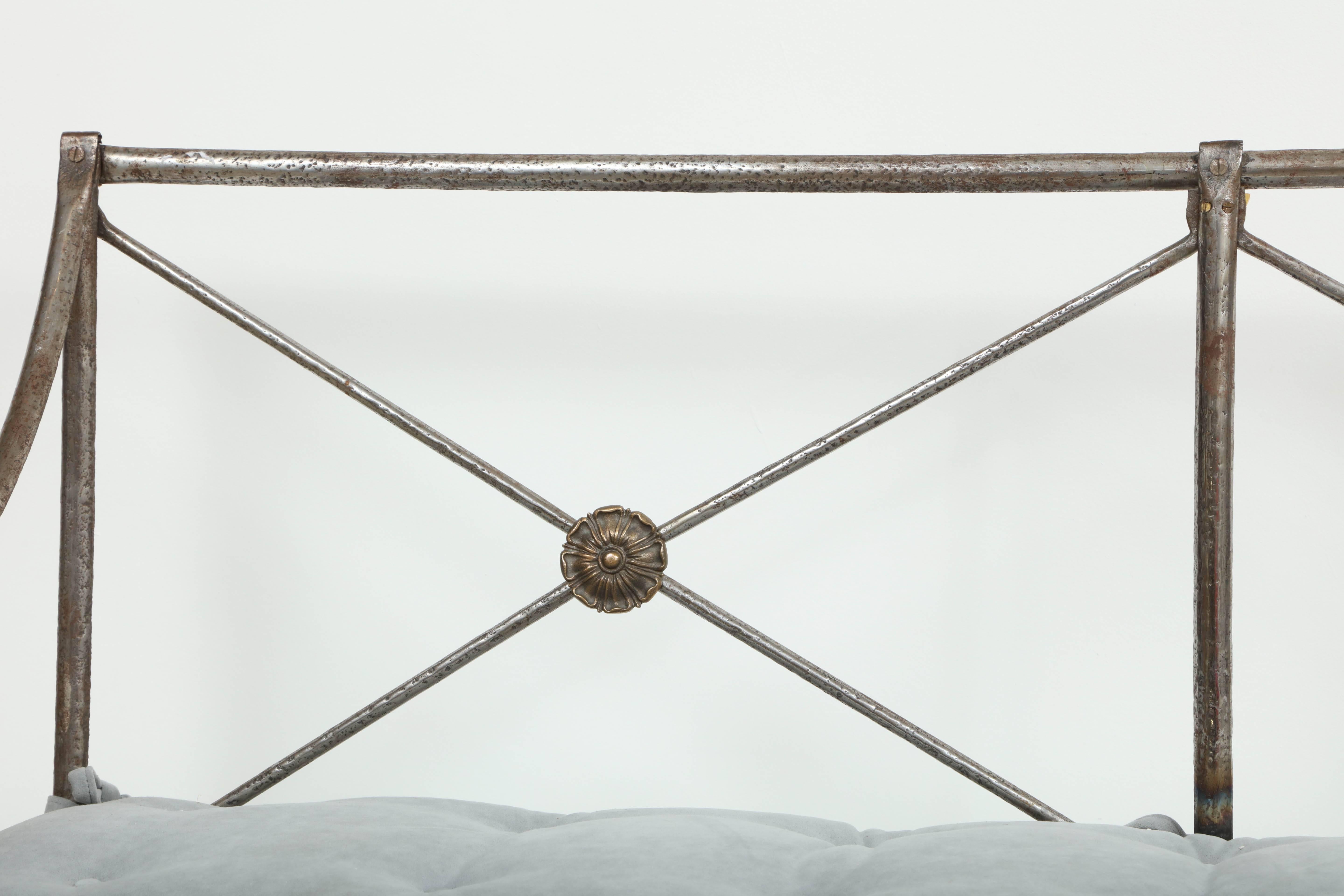 A chic bench in polished steel in the style of Maison Jansen, with X-form detail on back with bronze fleurettes, covered in a gray velvet, tufted cushion.