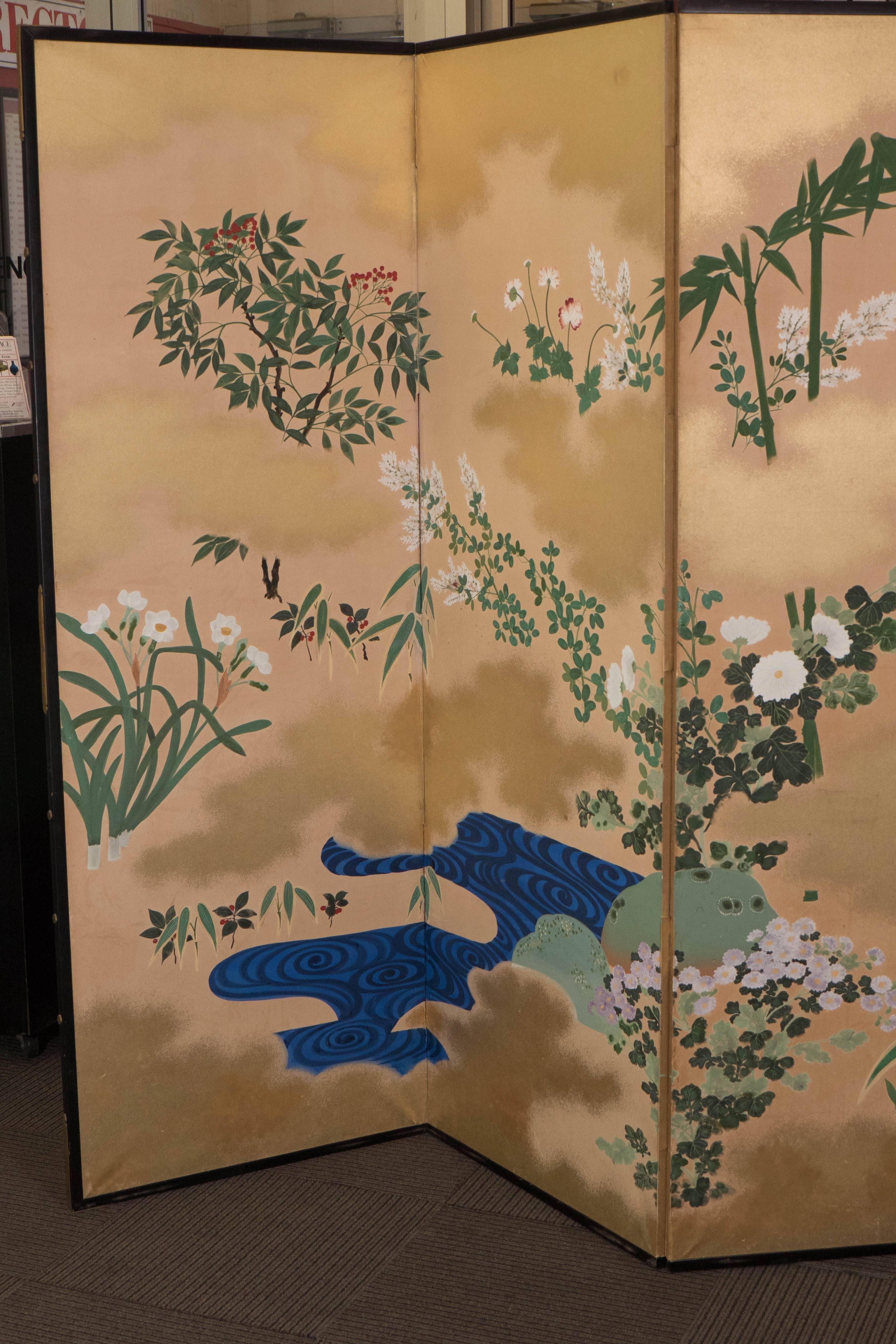 This six panel Japanese screen, produced early 20th century, amidst the late Meiji to early Showa period, comes set within a black lacquer frame, with paintings of various foliage, flowers and bamboo surrounding a blue lake, beautifully detailed