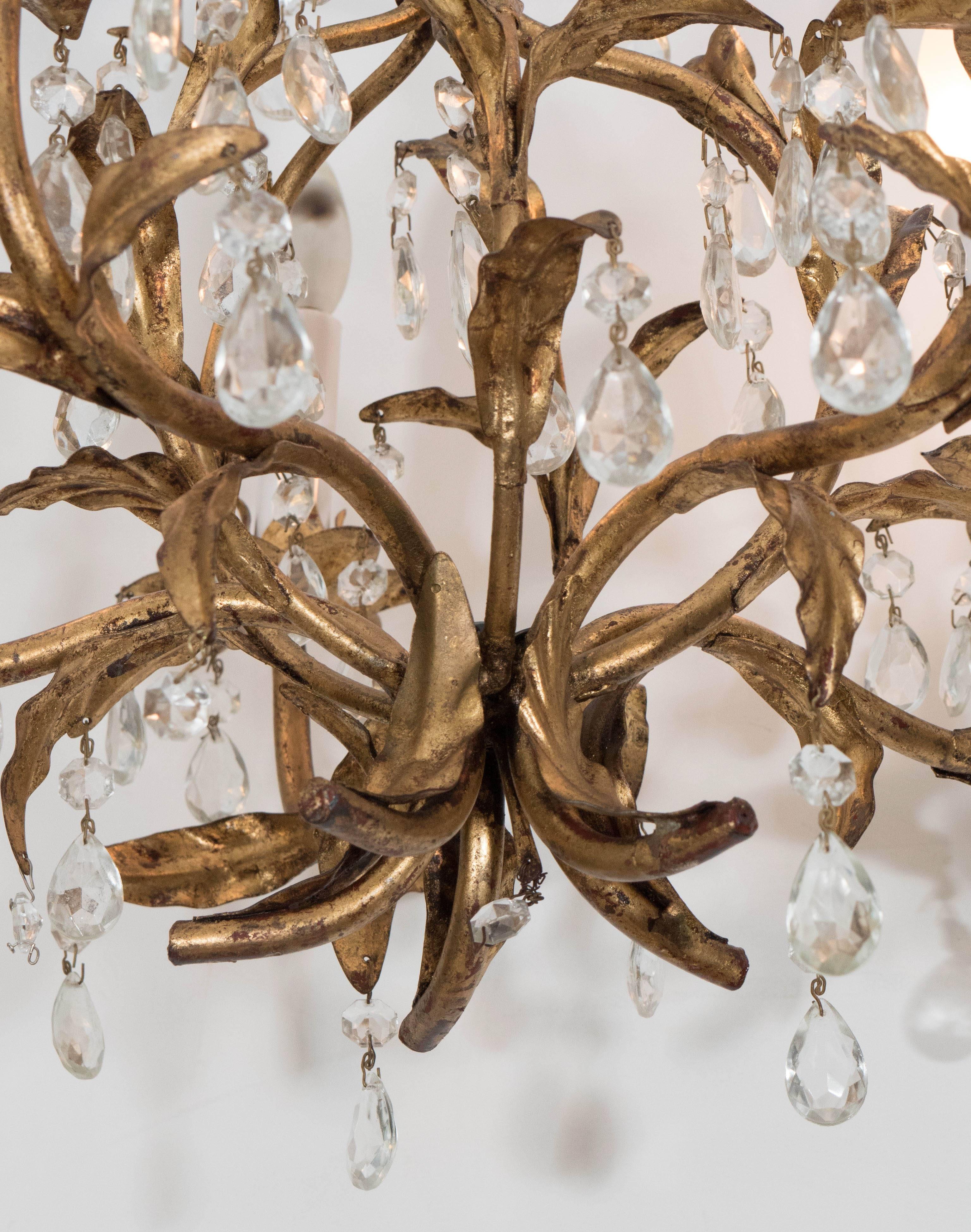 An Italian tole chandelier, produced circa 1940s, styled as a shaft of curved bound foliage, with five lights on curved stems, each with long socket covers and decorative flower shaped bobeches, entirely in warm gilded metal, trimmed with crystal