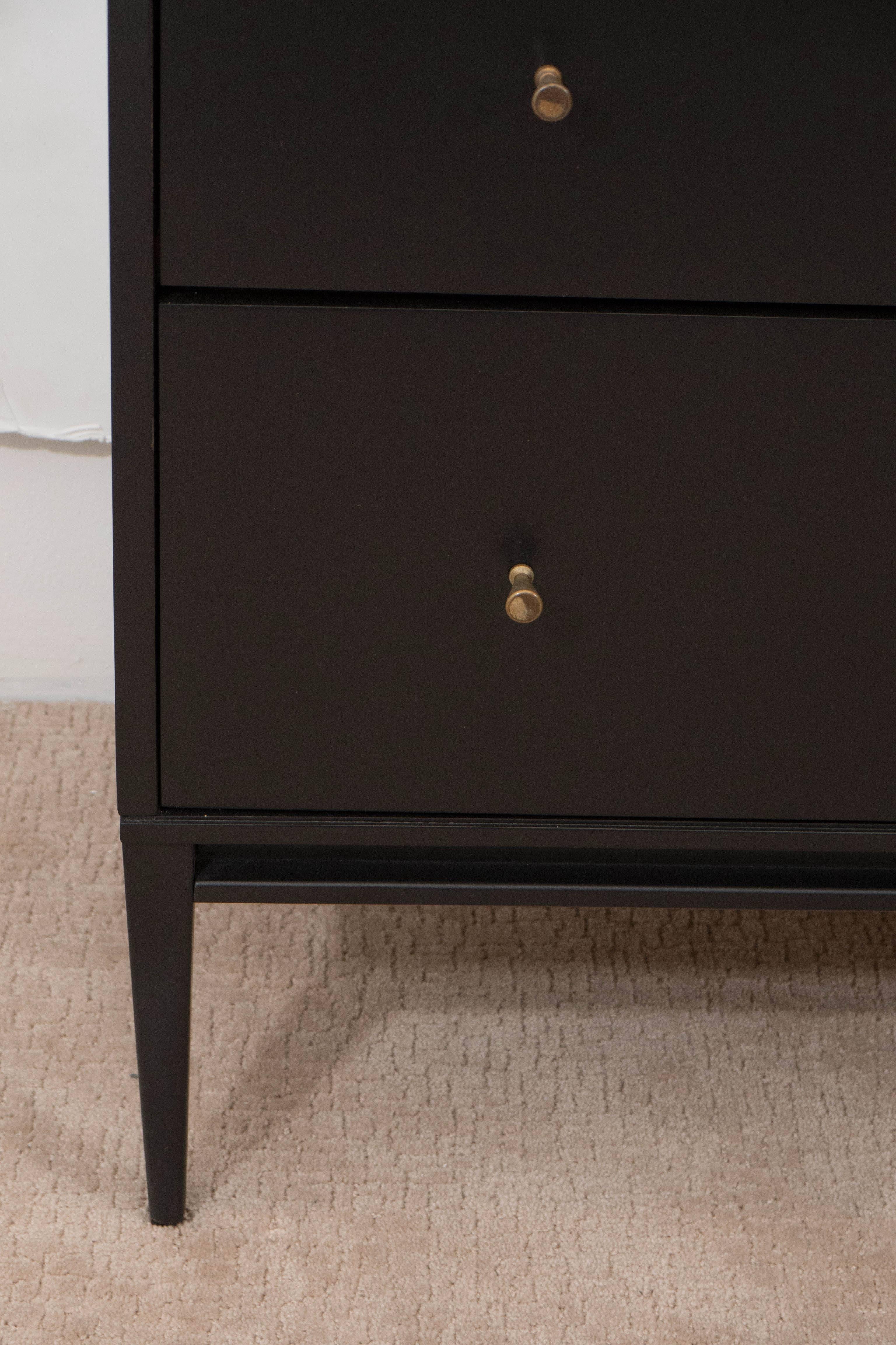 A four-drawer dresser by designer Paul McCobb, from the Planner Group line, produced by Winchendon Furniture Company circa 1950s, with black lacquer finish, brass pulls on lengthy square tapered legs. Markings include designer label [Planner Group,