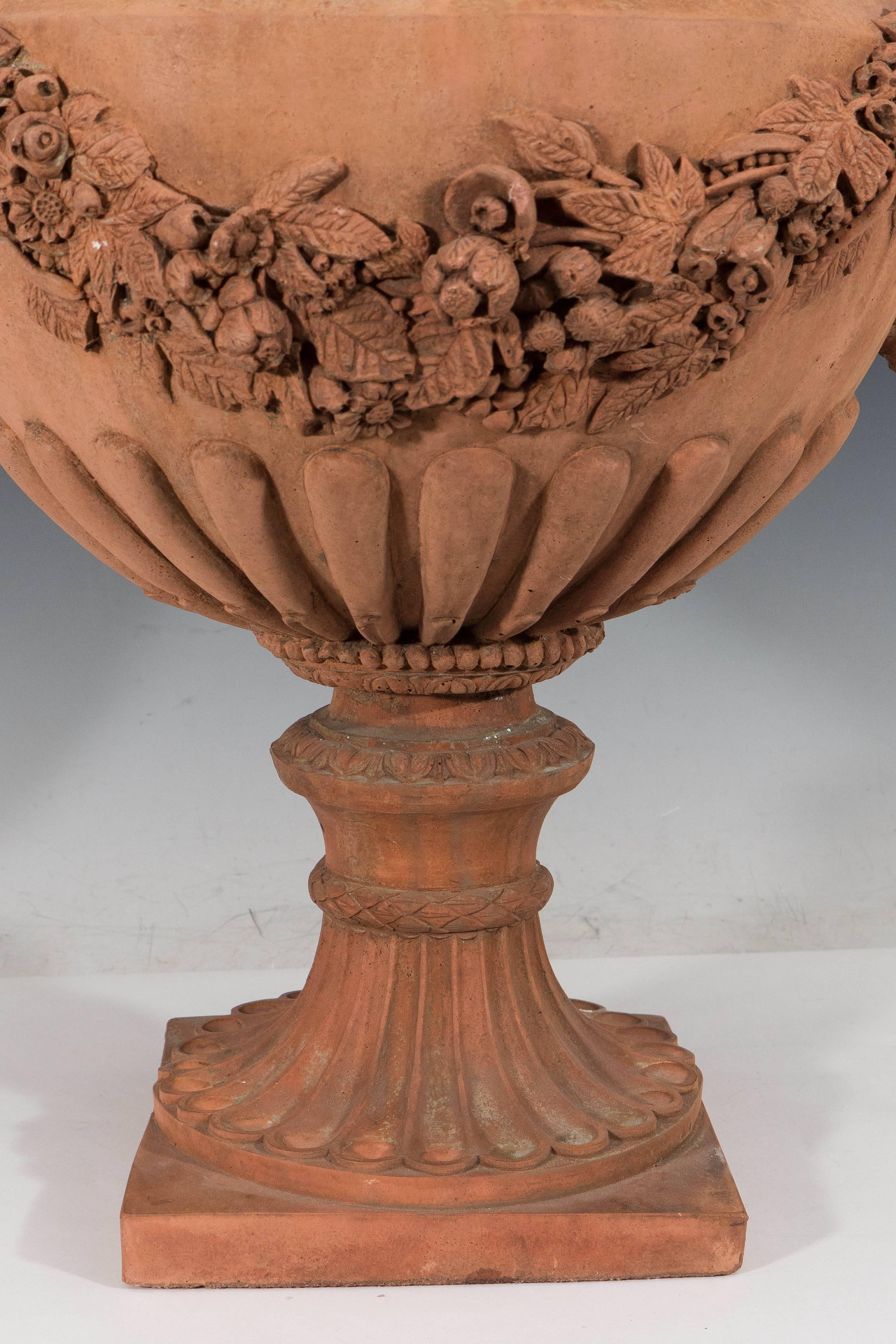This pair of neoclassical style terracotta planters and jardinieres, produced in Italy circa 1930s-1940s. Each come as a classical formed gadrooned urn, with rope motif and egg-and-dart border to rim, over intricately detailed floral festoons,
