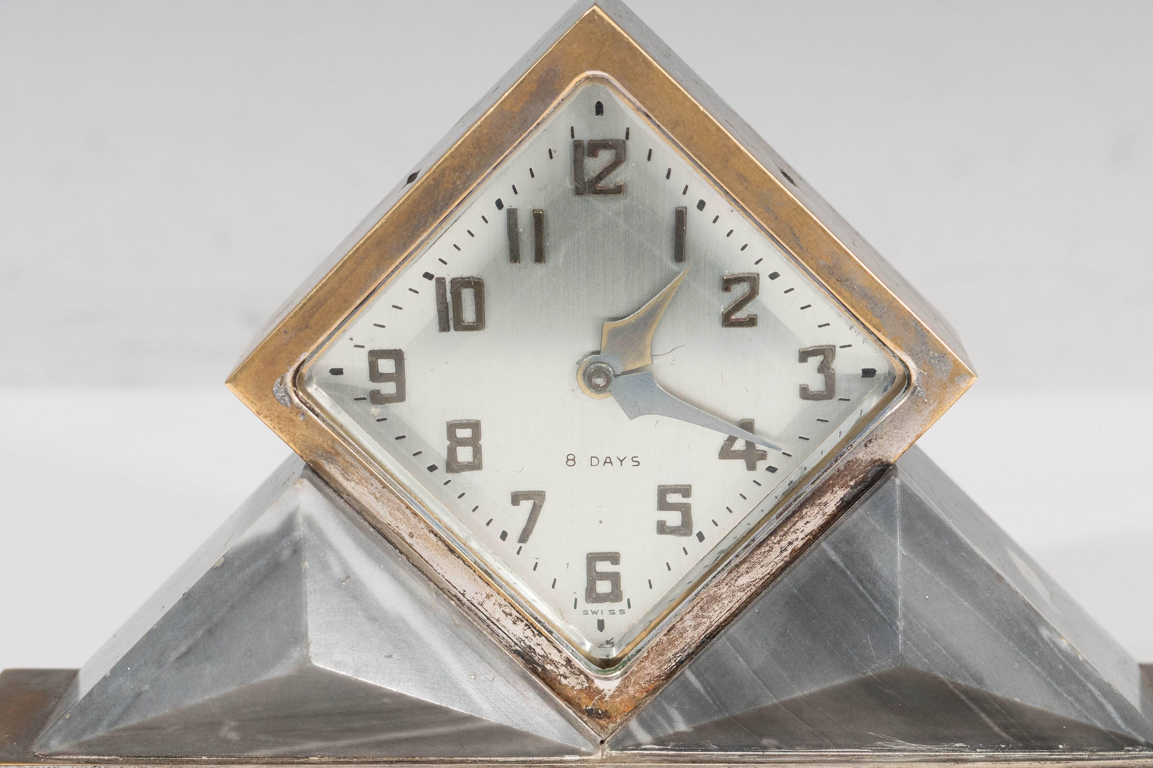 A vintage 8-day mantel clock, designed in the Art Deco taste by Omega, produced circa 1920s, with Arabic numerals, the face set inside a diamond form frame, flanked by two faceted grey marble triangles as supports, on stepped base. Markings include