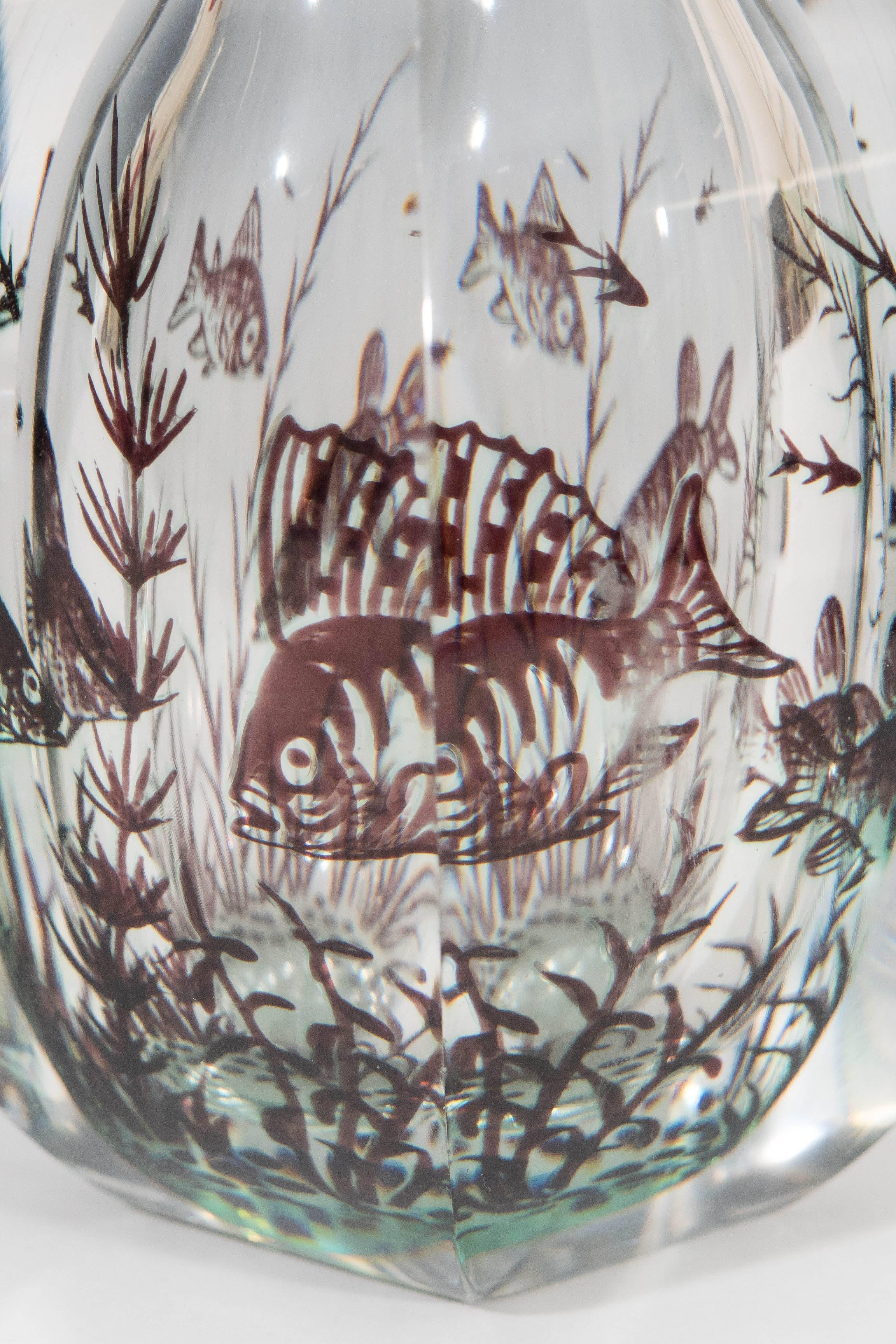 A thick, six-sided glass vase, produced circa 1950s-1960s by artist Edward Hald for Orrefors of Sweden, rendered using 'graal' technique (twice-blown), depicting seaweed and fish floating amidst crystal clear glass. Markings include