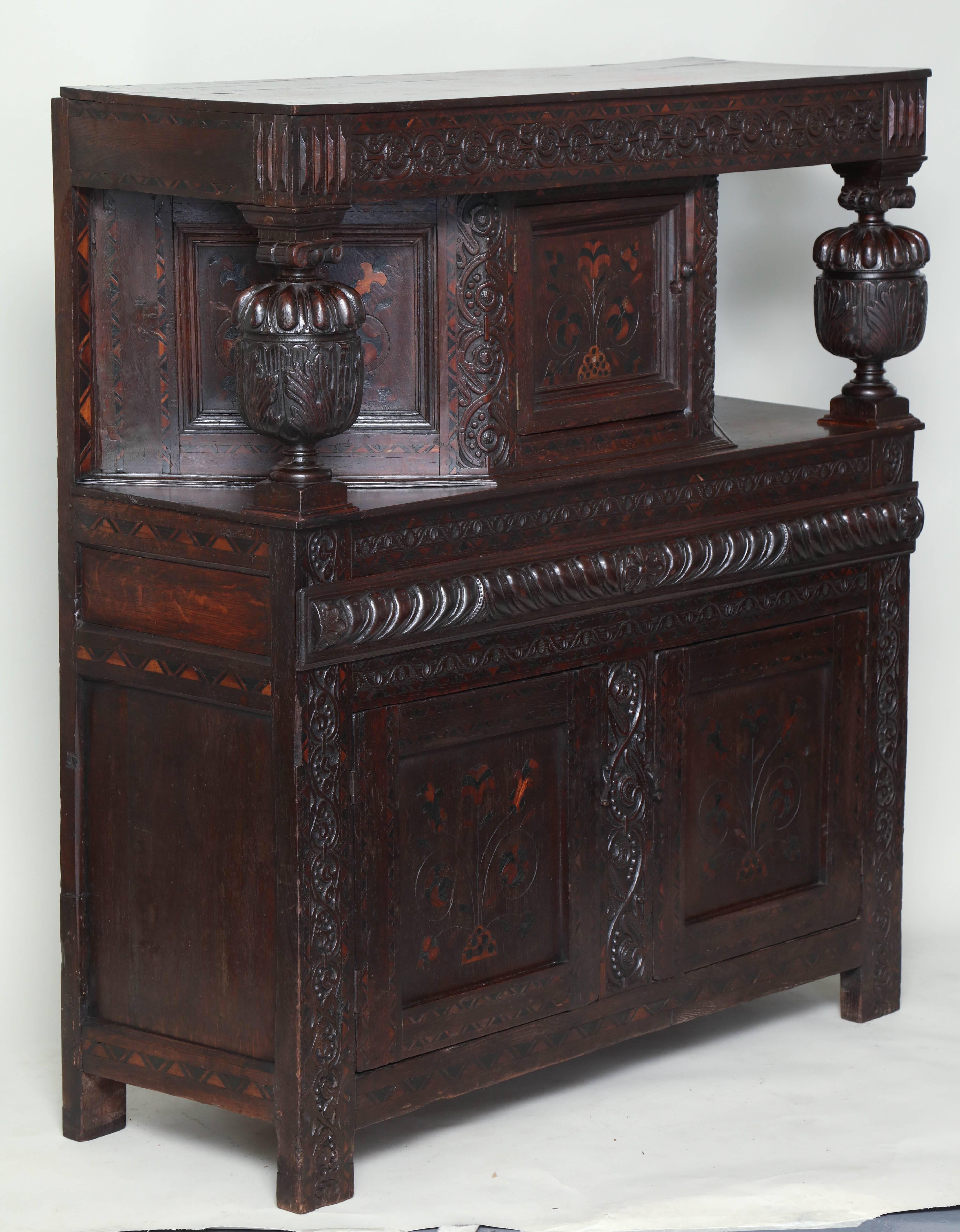 Very rare late Elizabethan inlaid oak court cupboard profusely carved and inlaid with sycamore and bog oak with arabesque chip carved frieze over rich cup and cover carved supports having canted cupboard in the upper section, two more arabesque