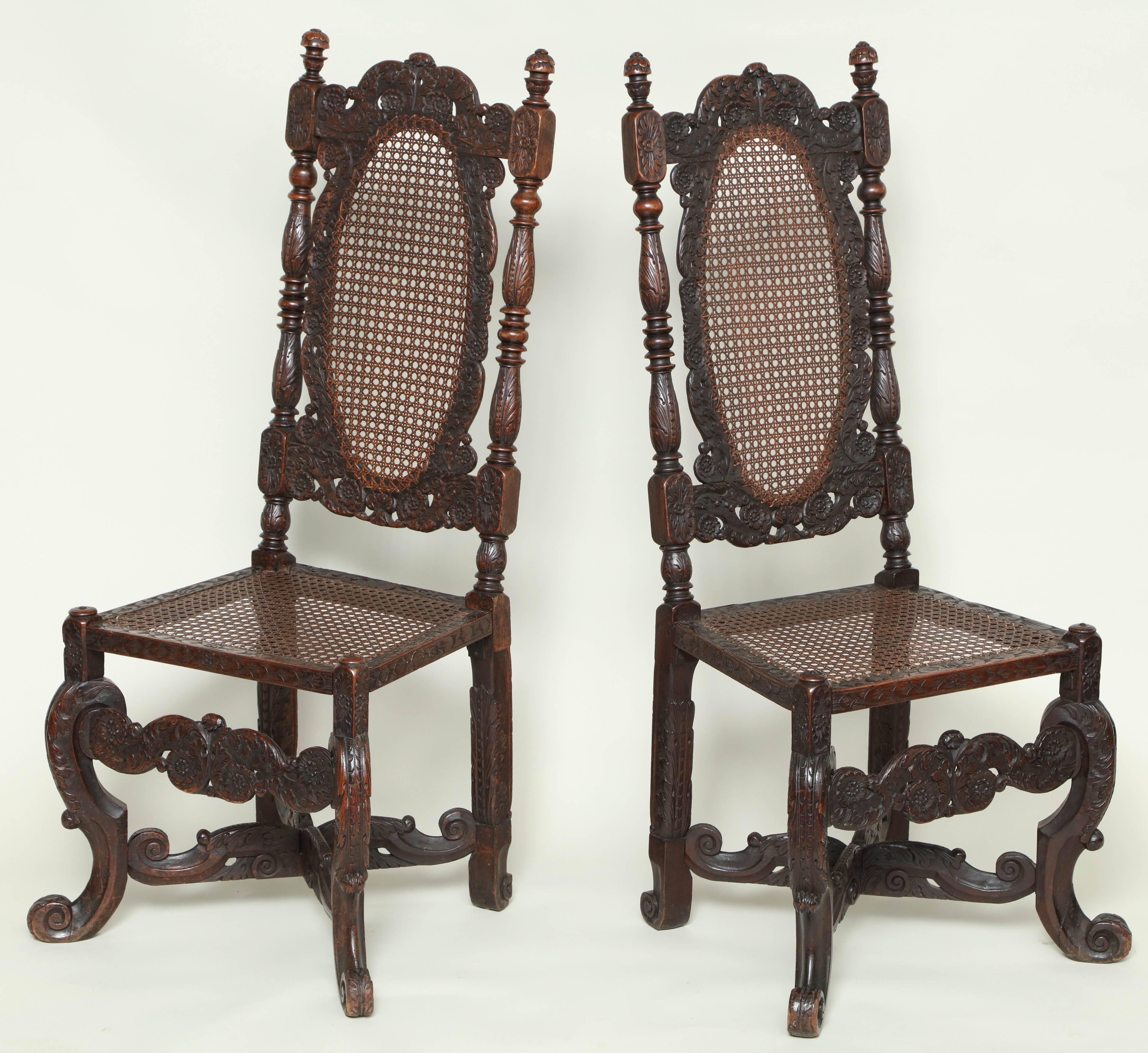 Fine and rare pair of James II walnut and cane hall chairs, the turned finials over profusely foliate carved oval backs with turned and carved uprights, standing on canted 