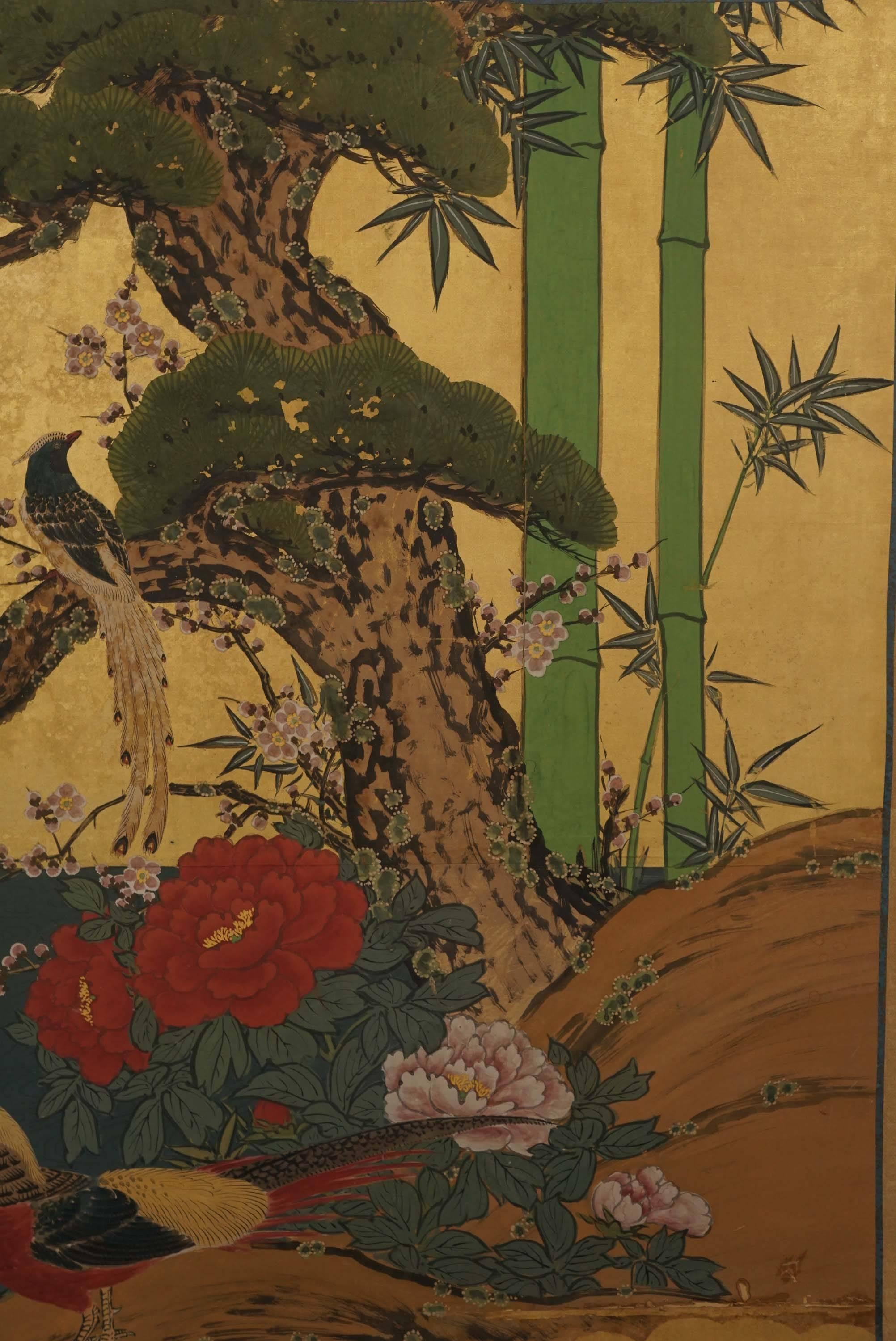 Two panel Japanese Screen from the Showa period depicting pheasant on a rock overlooking a pond bordered by pine tress, bamboo shoots and grasses. Ink and color on gold leaf paper. Fabric border and lacquered frame. 