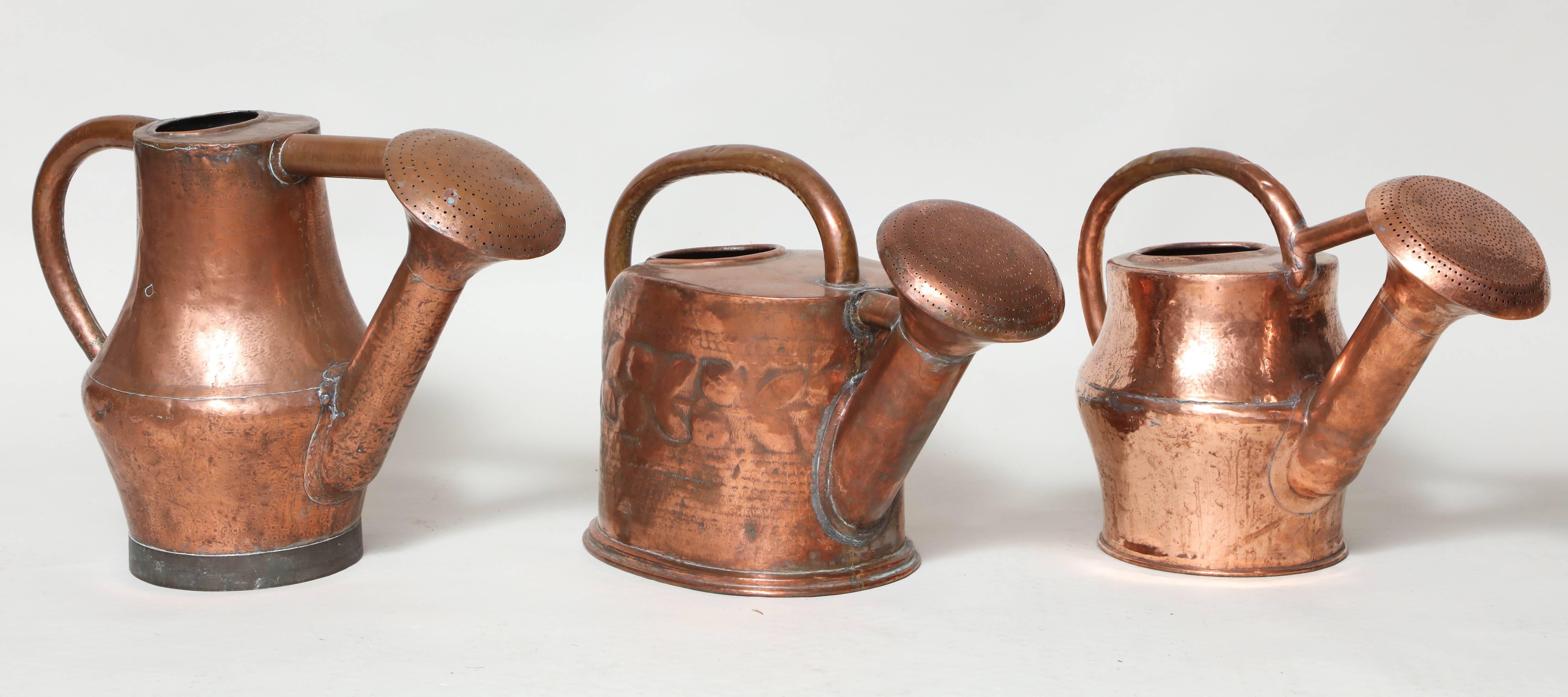 Three watering cans in hand-hammered copper with organic forms and large rose-heads, having seamed construction and impressed shape decoration, French, 19th century.