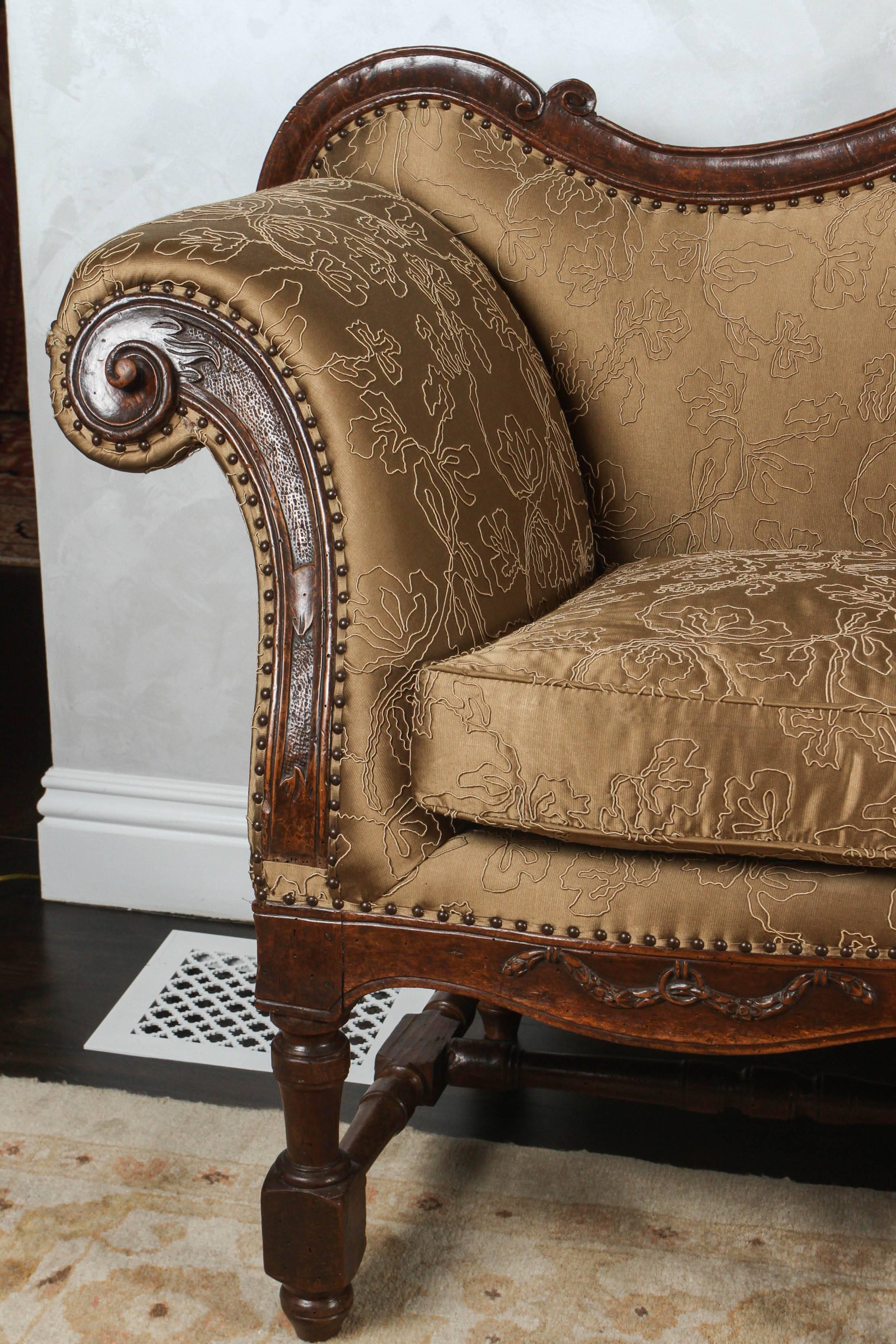 18th century French carved walnut canapé sofa with stretcher. There are eight beautifully turned and pegged legs. The sofa has a garland swag motif. It has been finished with nail heads and is newly upholstered in a golden/bronze silk fabric.