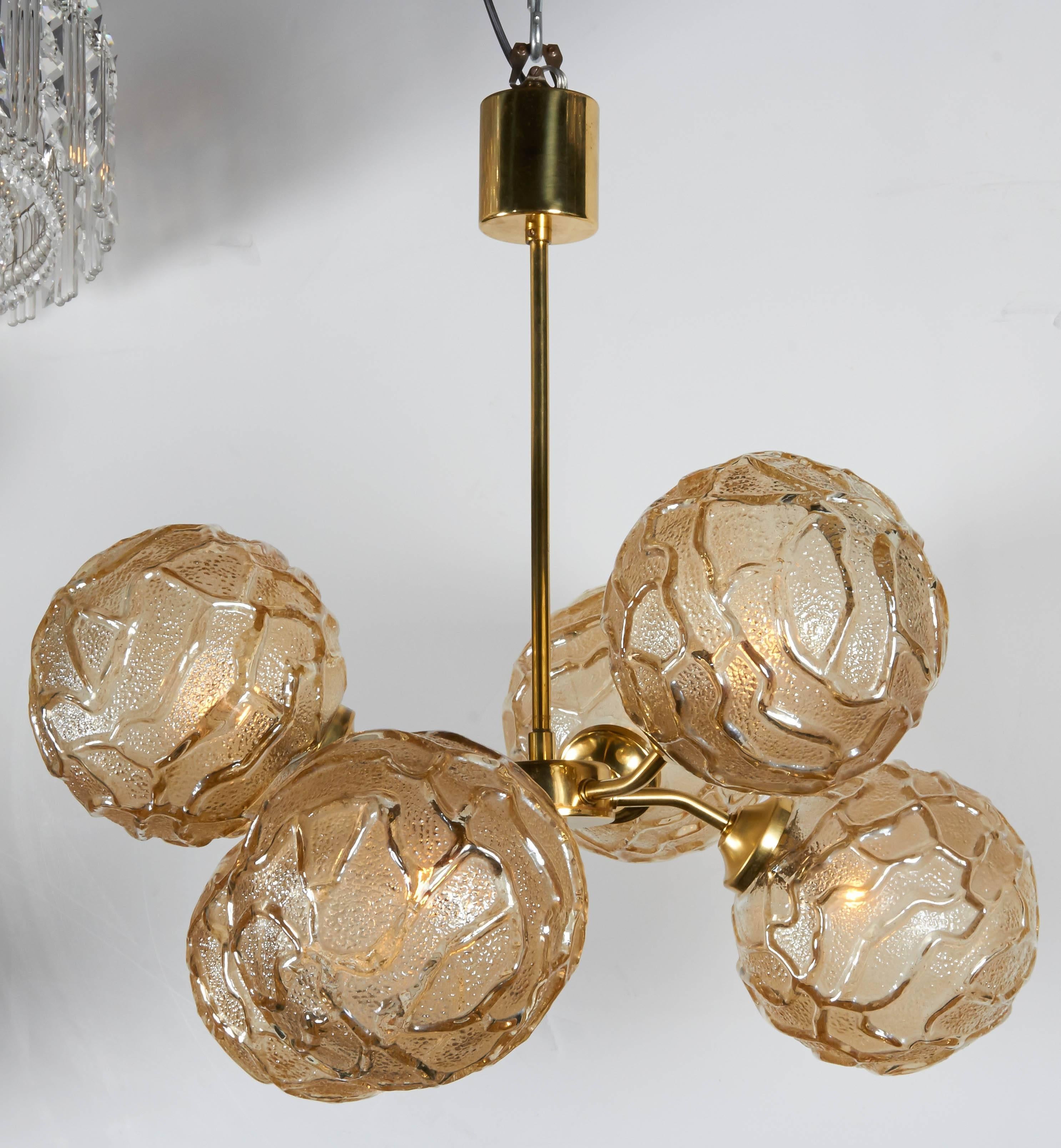 Mid-century modern sputnik globe chandelier with brass atomic frame design. The fixture has an elegant stem and cylinder canopy, with alternating arm design.  Fitted with six textured art glass globes with geometric patterns in hues of champagne or
