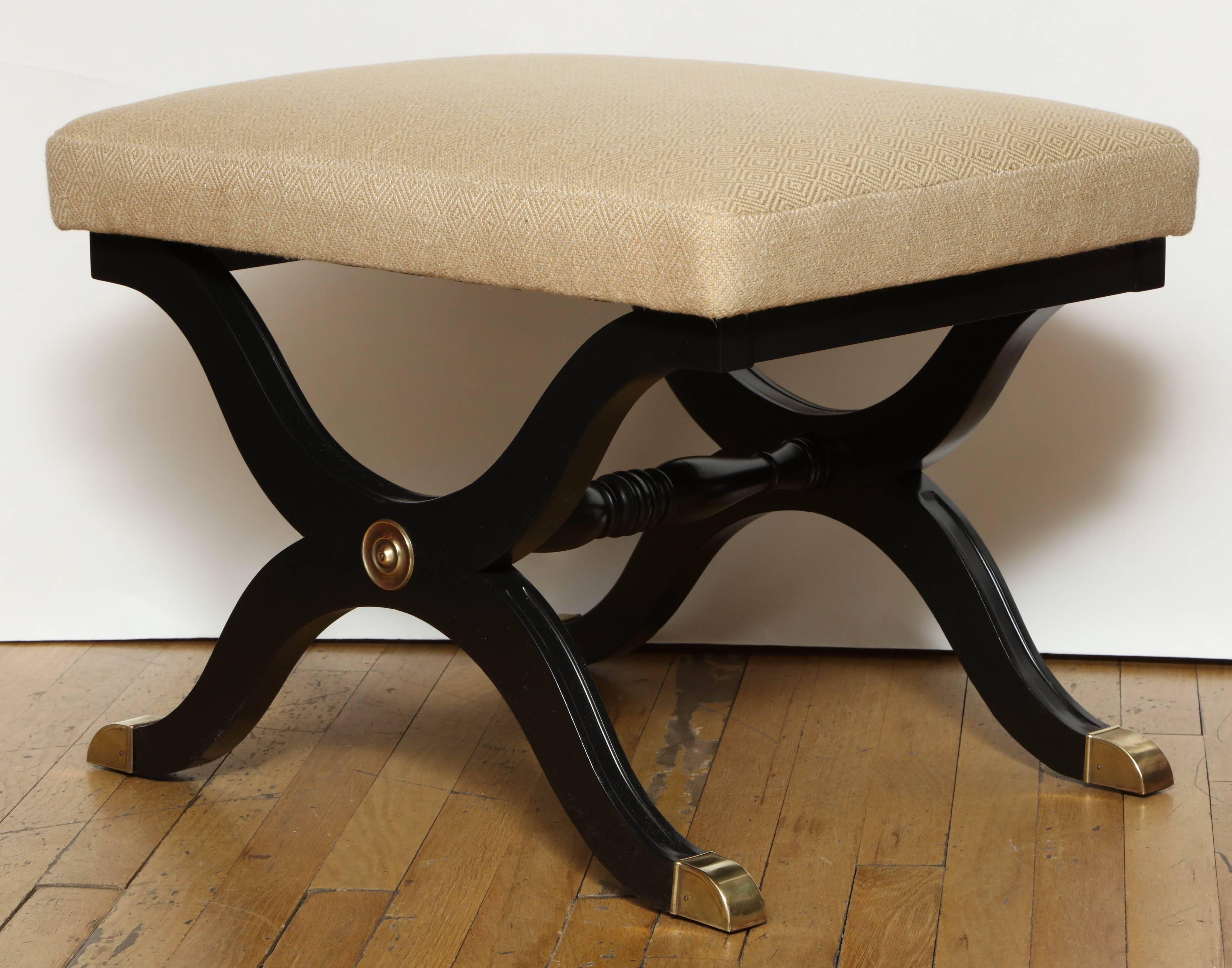 A Regency inspired curule X frame bench, the four splayed legs terminating in metal caps, joined by turned stretcher. The seat with boxed upholstery. 