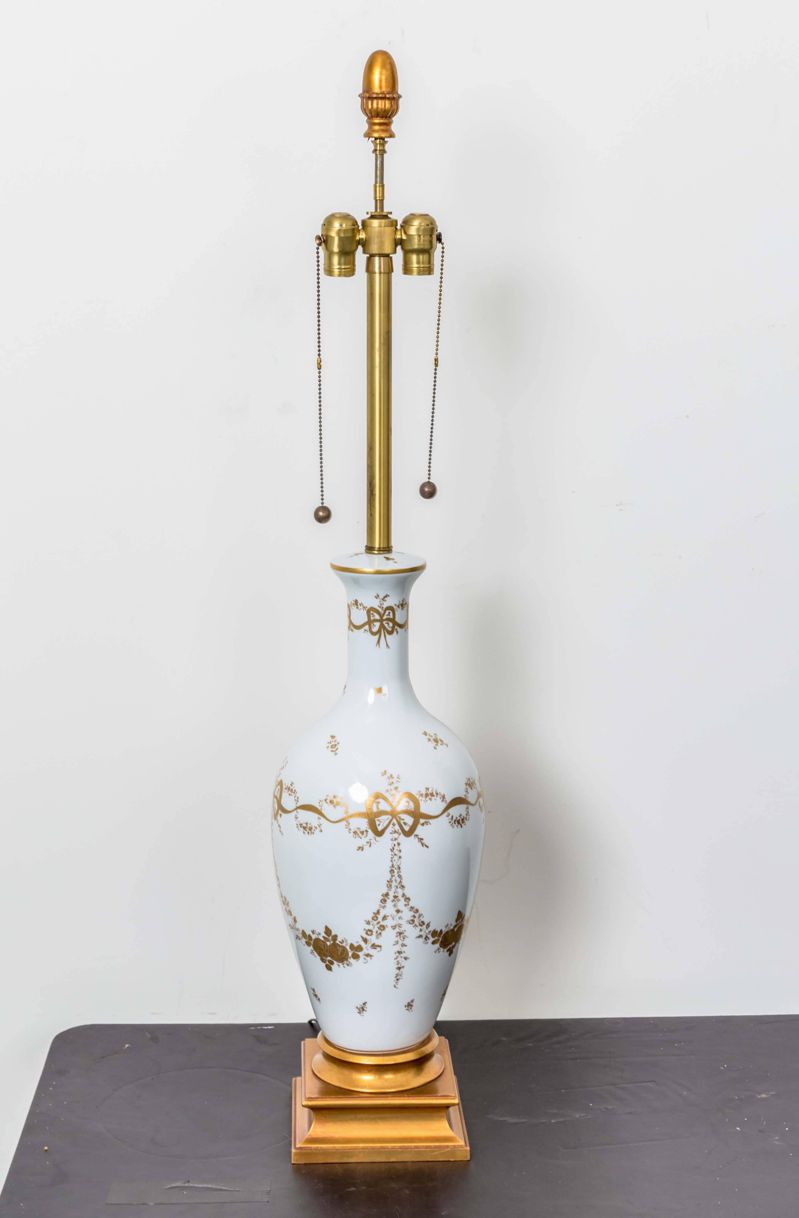 Vase shaped white porcelain table lamps with gold garland, bows and ribbons. In the manner of Le Tallec; Paris on wood bases.