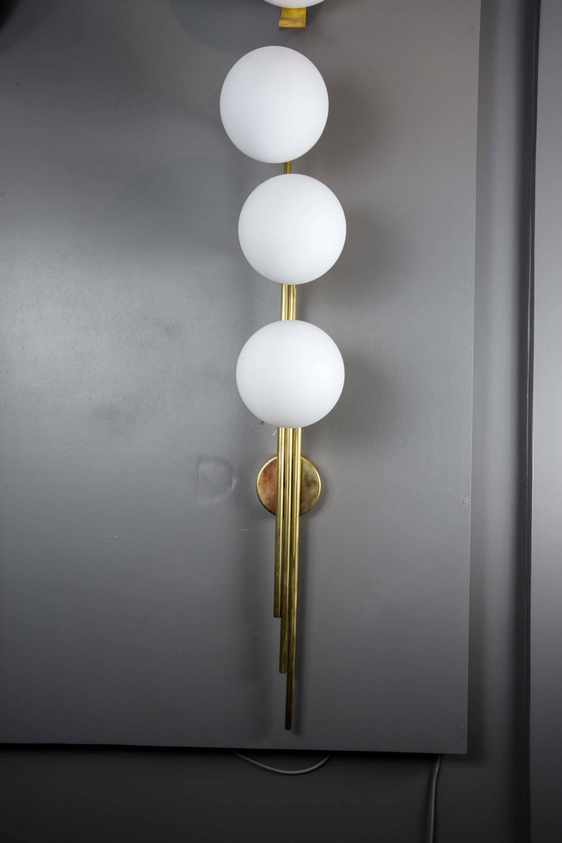 Set of six tall wall sconces made of a brass structure supporting three large white glass globes.