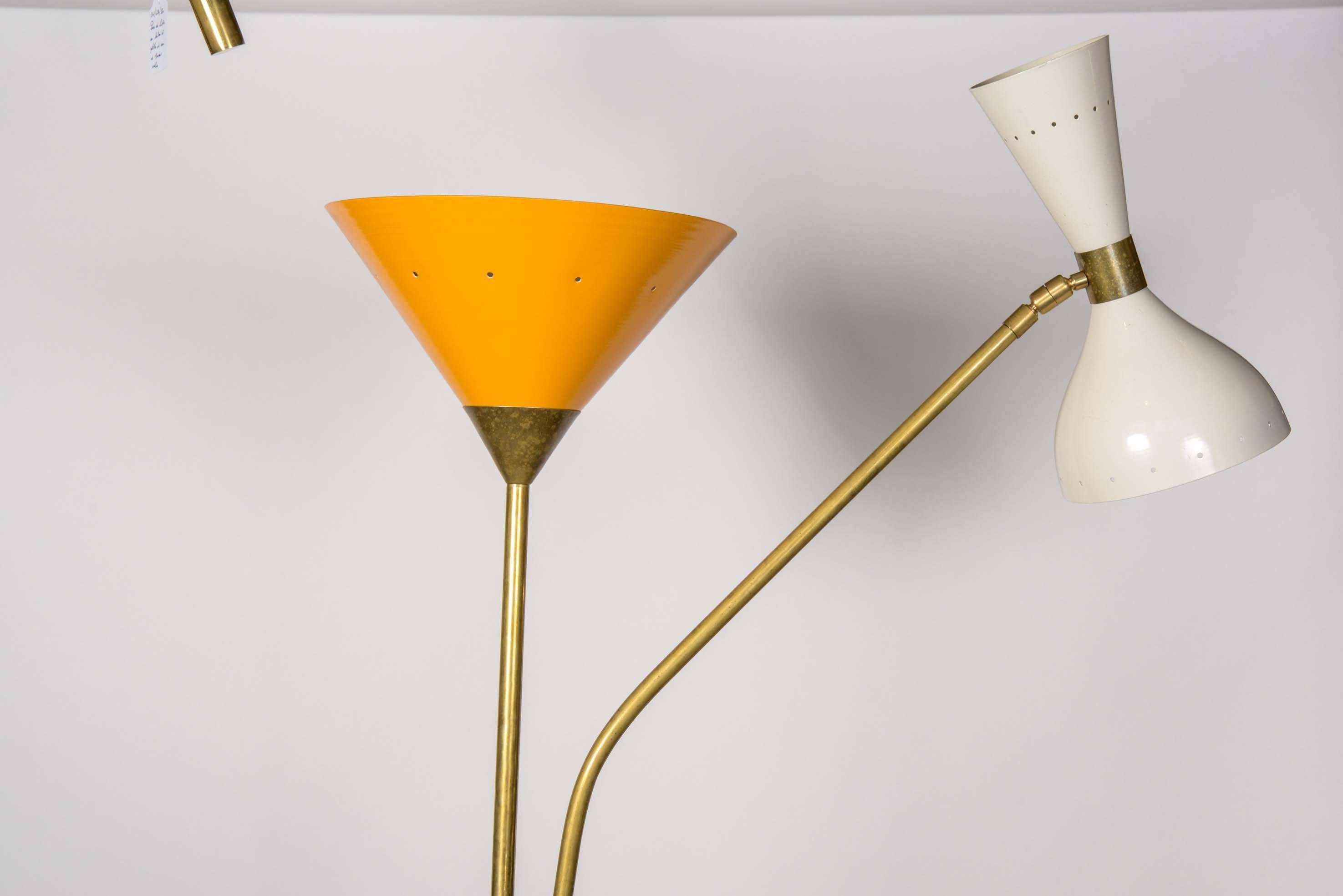 Floor lamp made of a white marble foot, two long brass arms, one ended by a yellow cone and the other one by the typical two sides sconce popularized by Stilnovo in a white colorway.

While the arm with the yellow cone remain vertically still, the