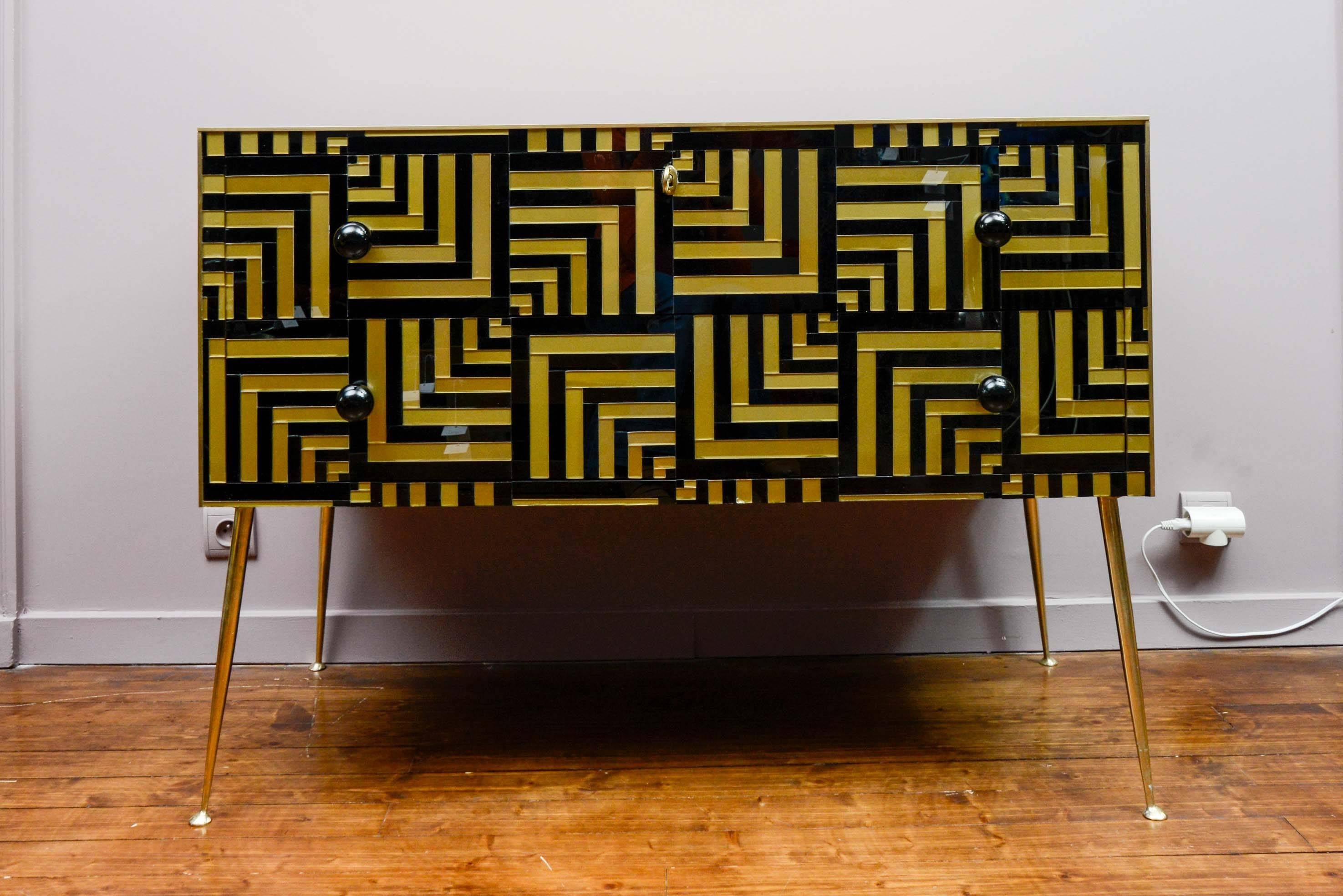 Pair of vintage chests of drawers, geometrical black and gold designs on the doors, four brass feet, two drawers.