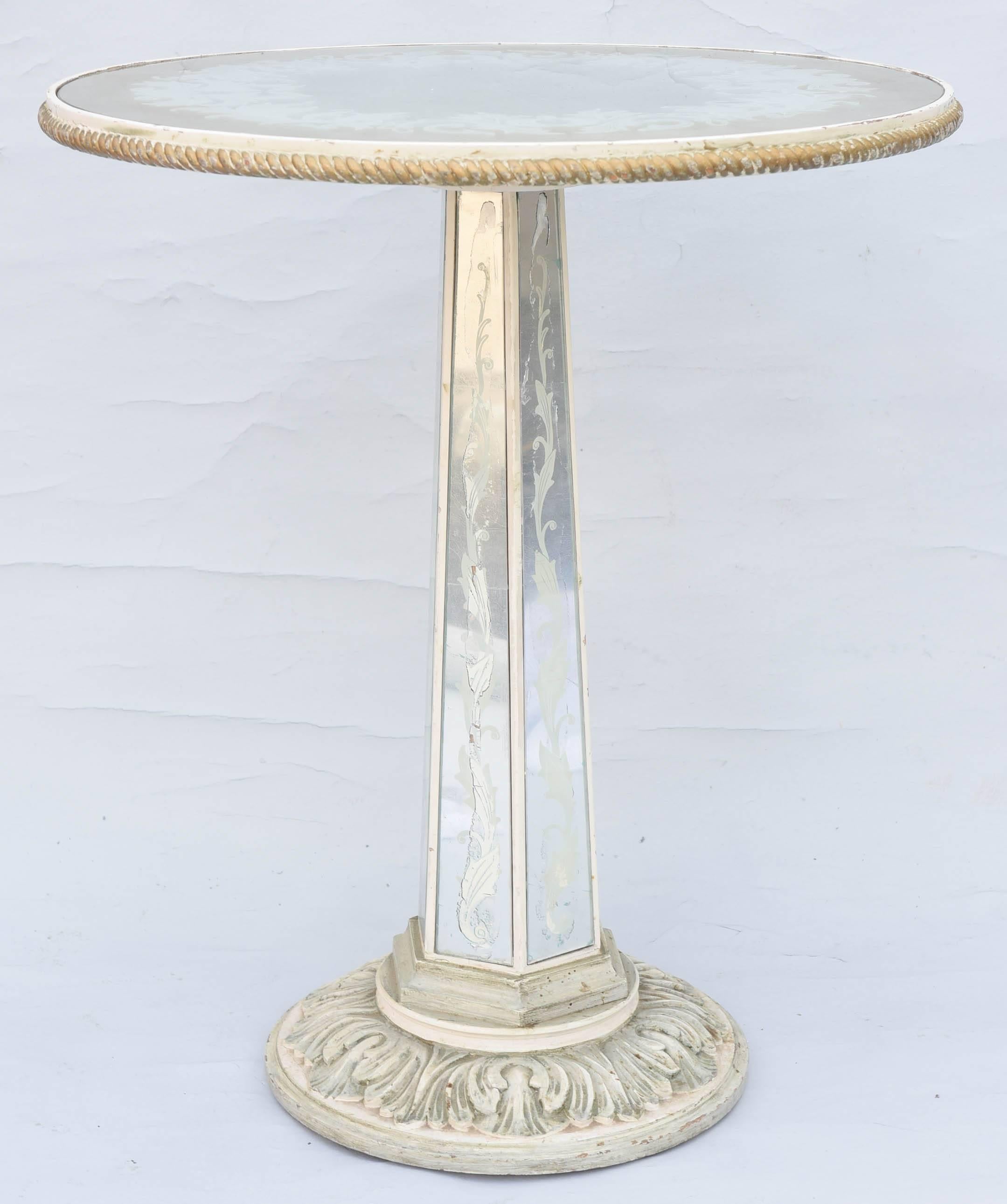 Occasional table, having a painted finish with natural wear, its round, églomisé, mirrored top, with a scrolling, foliate design of gold over silver, rope-carved, gadrooned edge, raised on hexagonal pedestal base, inset with etched mirror, on