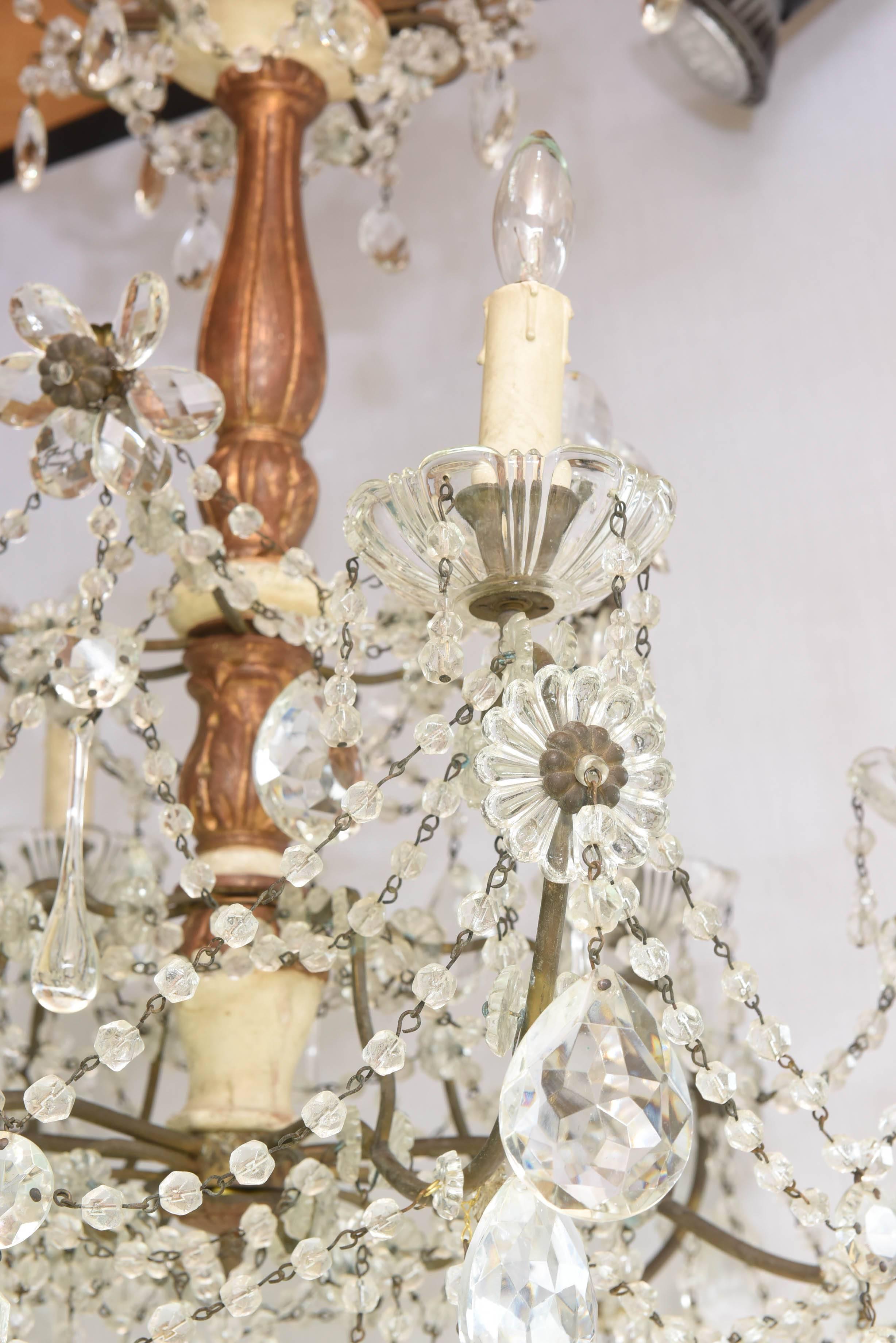 Chandelier, having a central column of an 18th century carved giltwood pricket stick, extruding four tiers of bronze arms, draped with strands of crystal beaded chains, six S-scroll candle arms ending in scalloped bobeches, and electrified candles,